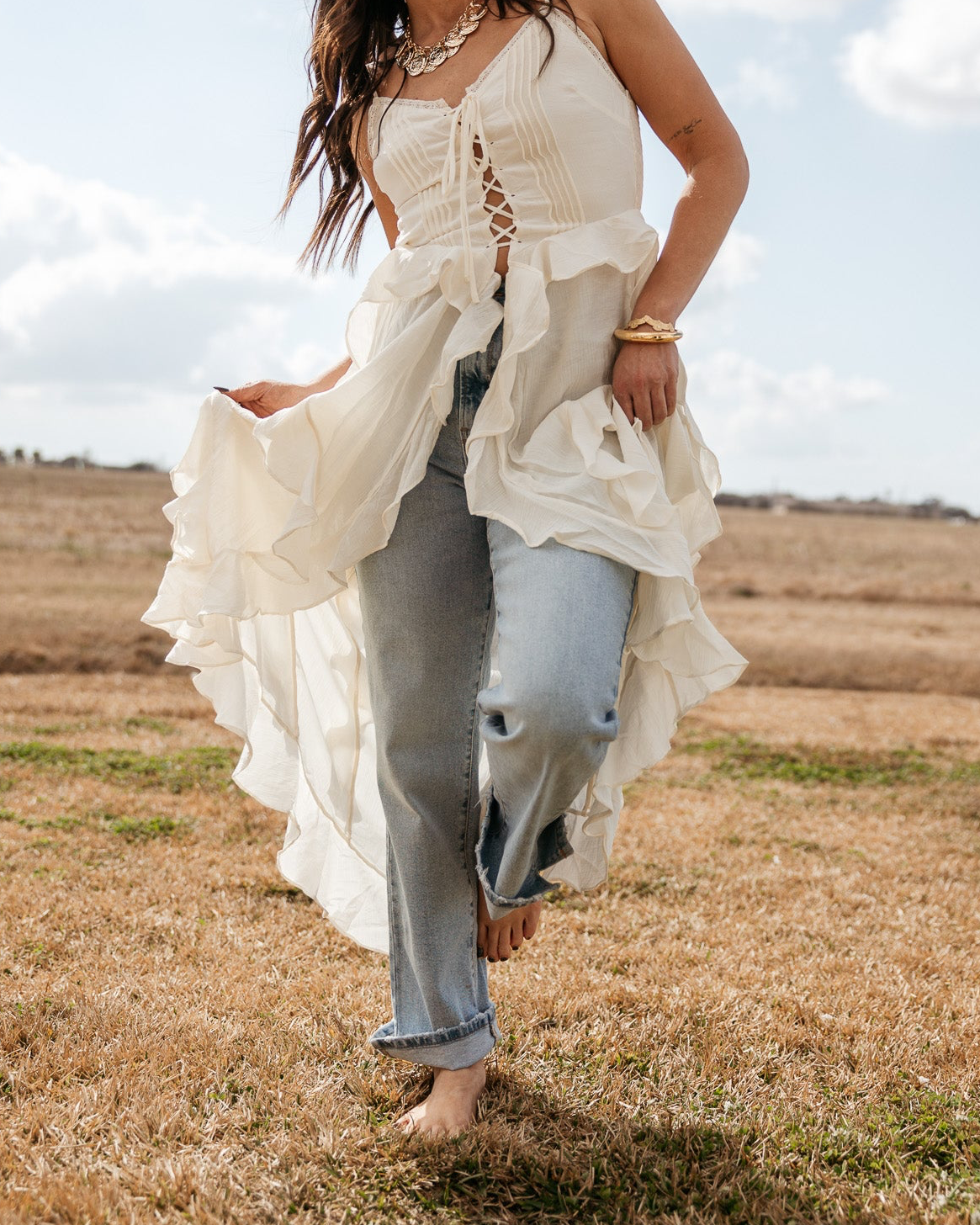 Woman in western boho outfit with flowy white top, blue jeans, and cowboy hat outdoors
