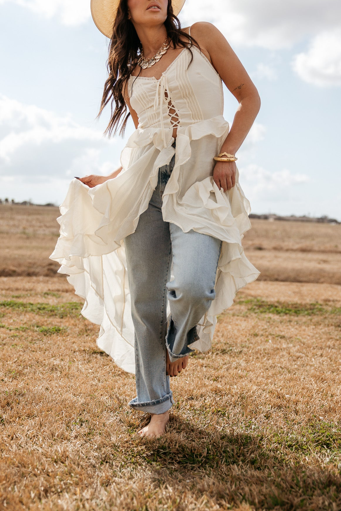 Woman in western boho outfit with flowy white top, blue jeans, and cowboy hat outdoors