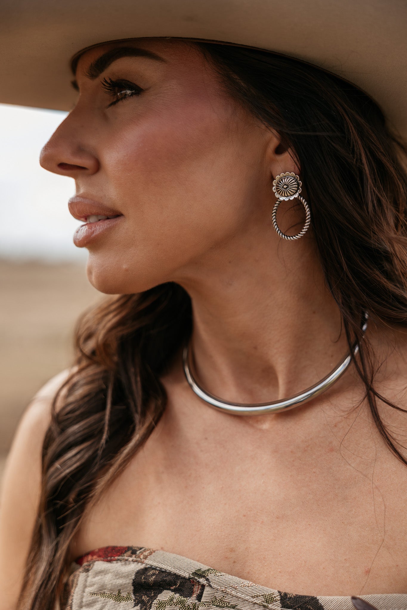 Woman in cowgirl hat wearing silver chunky necklace and floral hoop earrings, western fashion