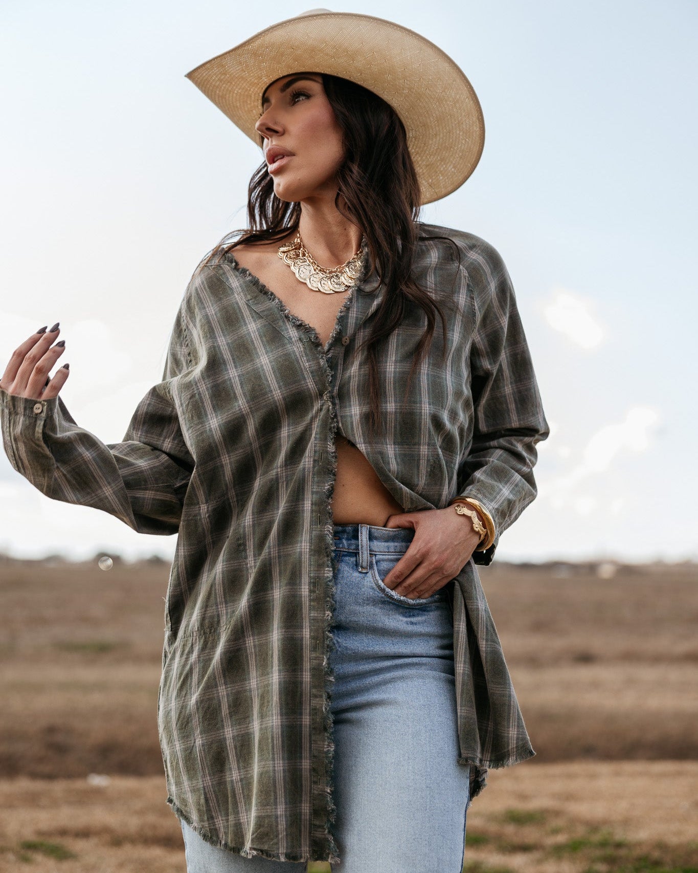 Woman in a straw cowboy hat, plaid western shirt, and distressed jeans outdoors