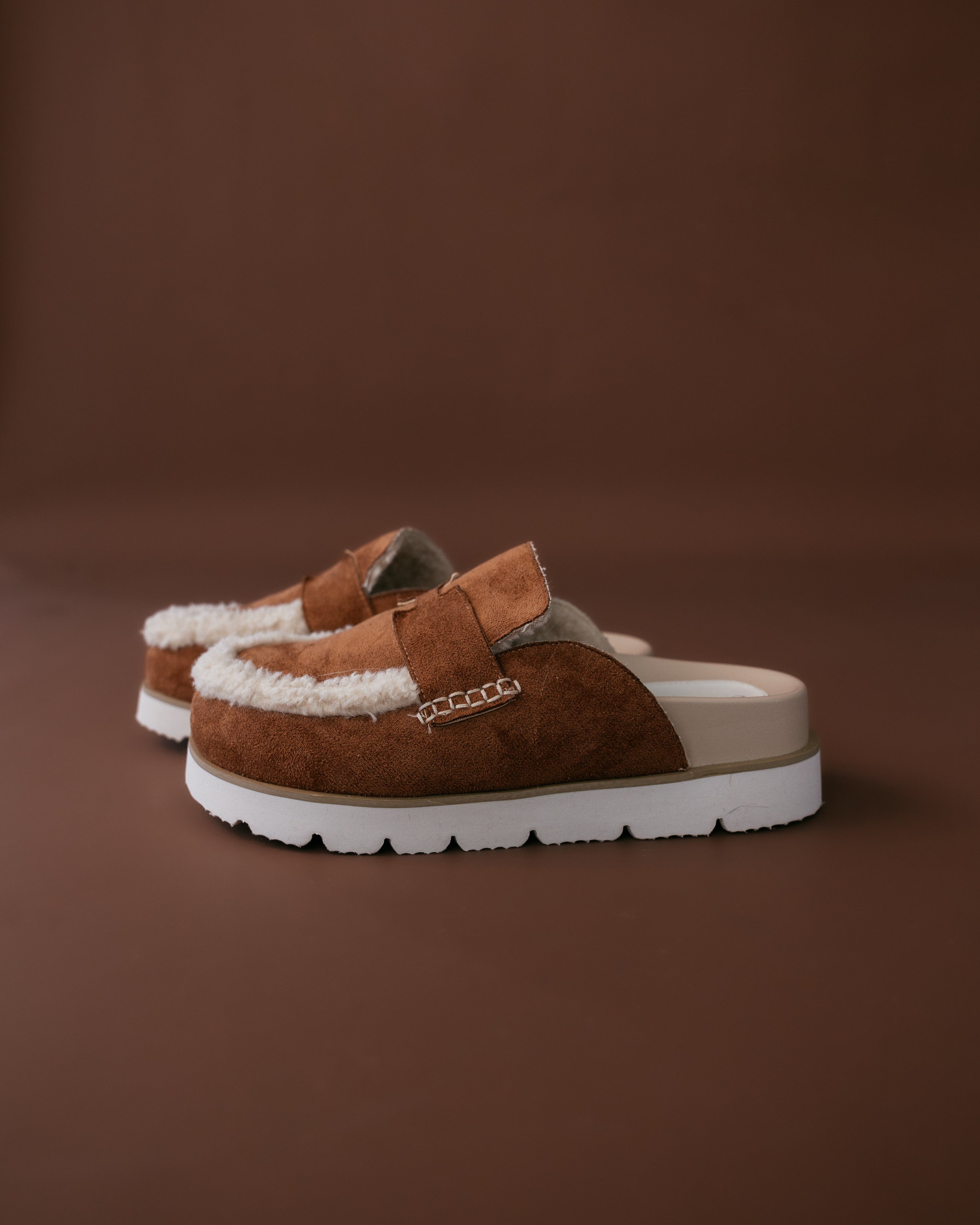 Pair of brown suede shoes with white soles on a brown background