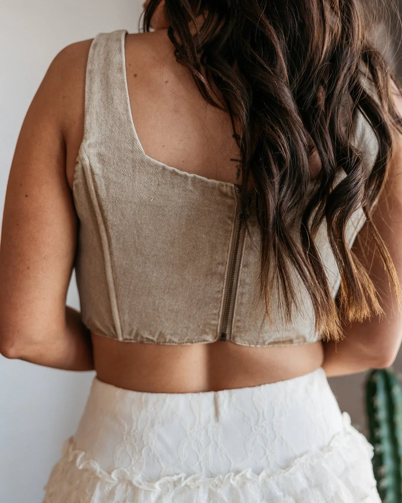 Woman wearing a beige sleeveless top and white skirt with braided hair.