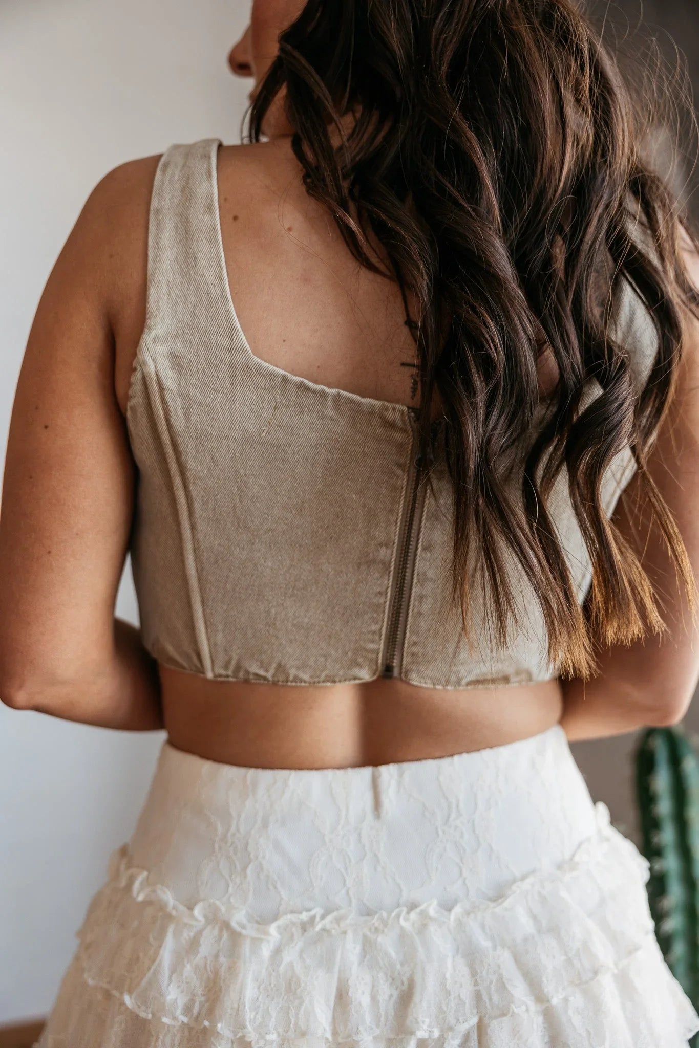 Woman wearing a beige sleeveless top and white skirt with braided hair.