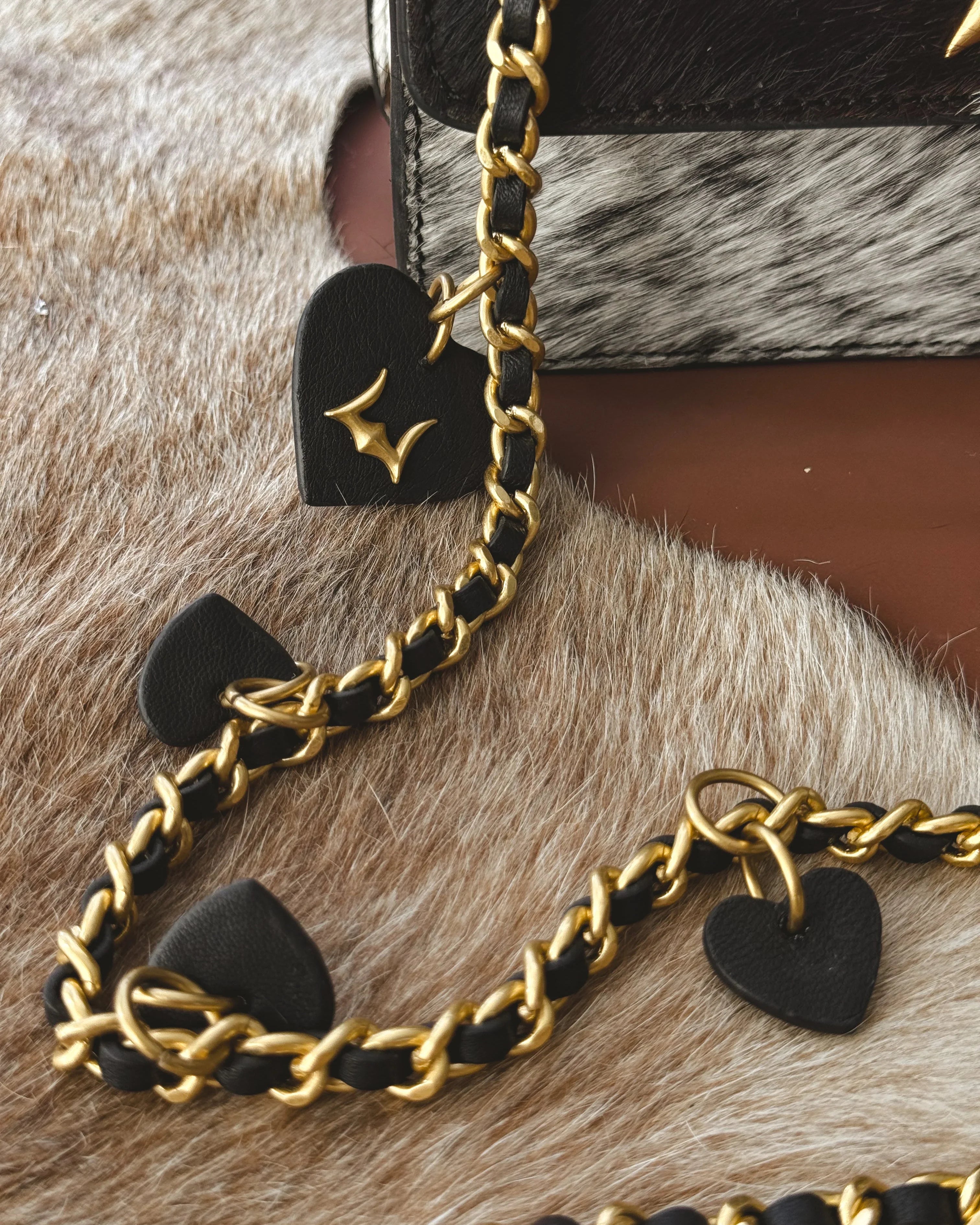 Gold chain with black heart-shaped pendants on a textured surface