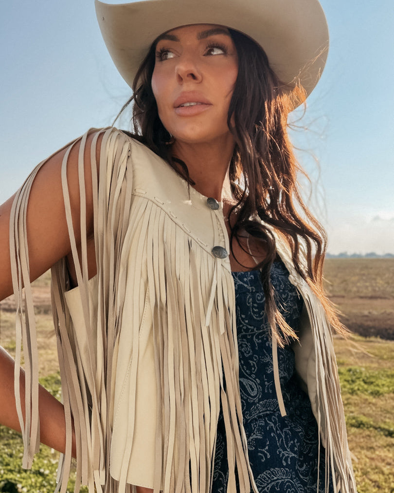 Woman in a cowgirl hat and fringe suede vest wearing a western boho dress outdoors