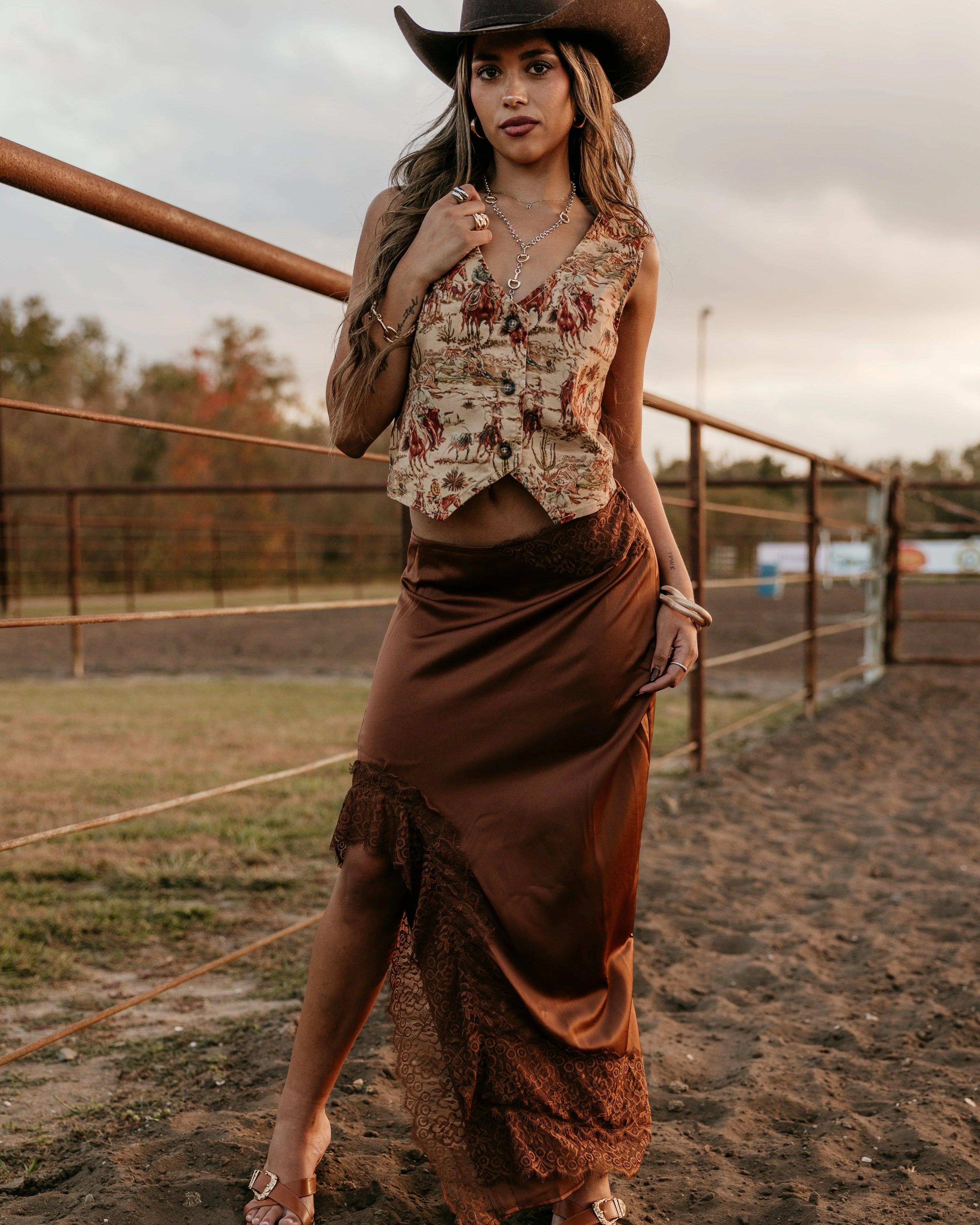 Woman in a cowboy hat and rustic outfit standing in an outdoor setting.