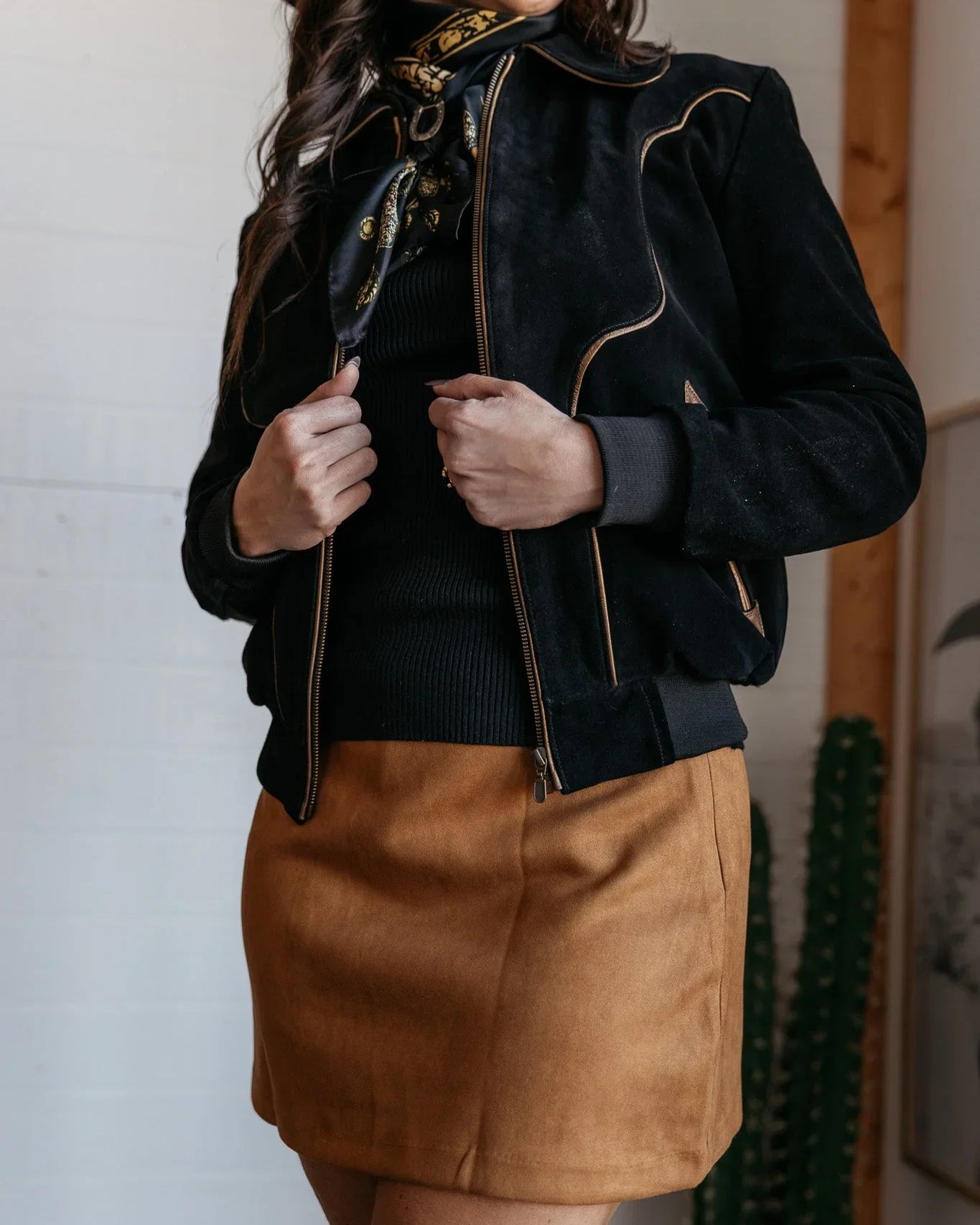 Woman in western boho outfit with black suede jacket, brown mini skirt, and black hat
