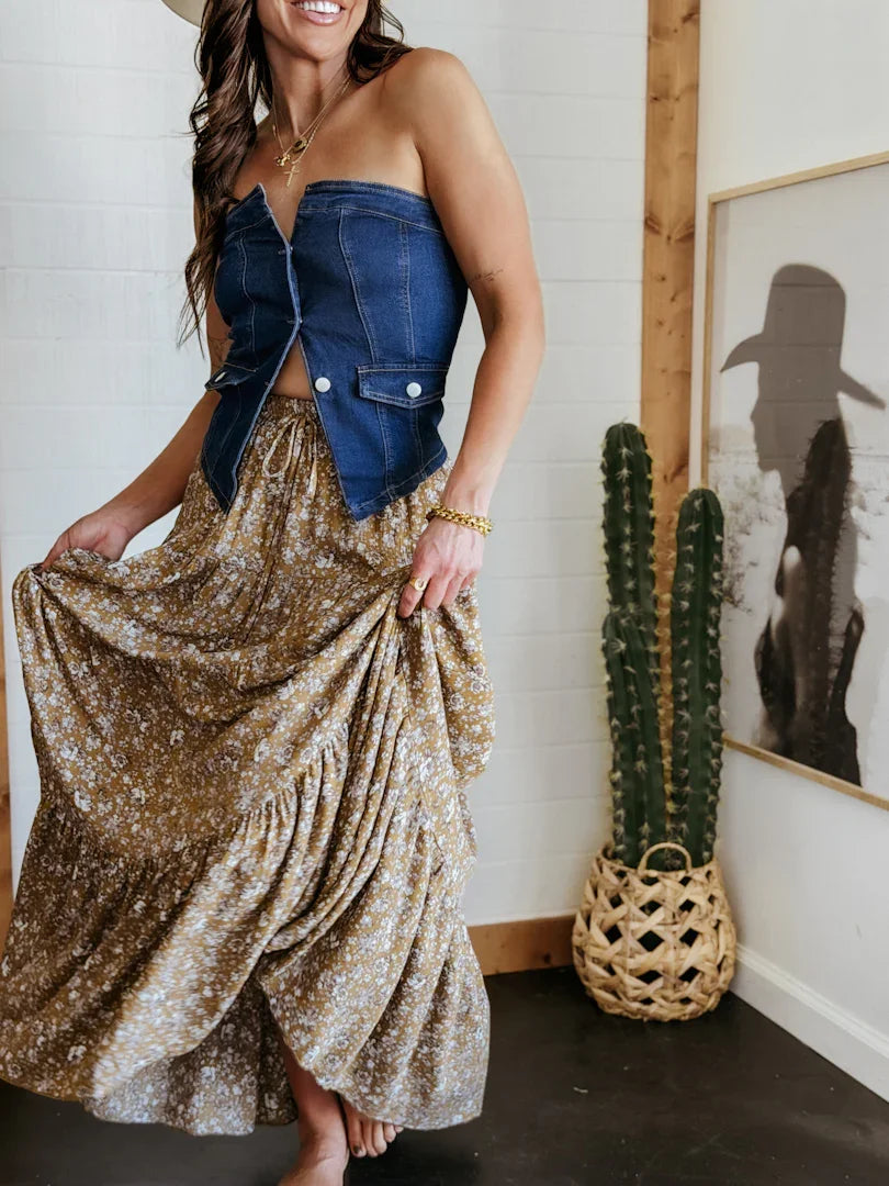 Woman wearing a denim vest over a gold sequin dress in a room with a cactus plant and framed picture.