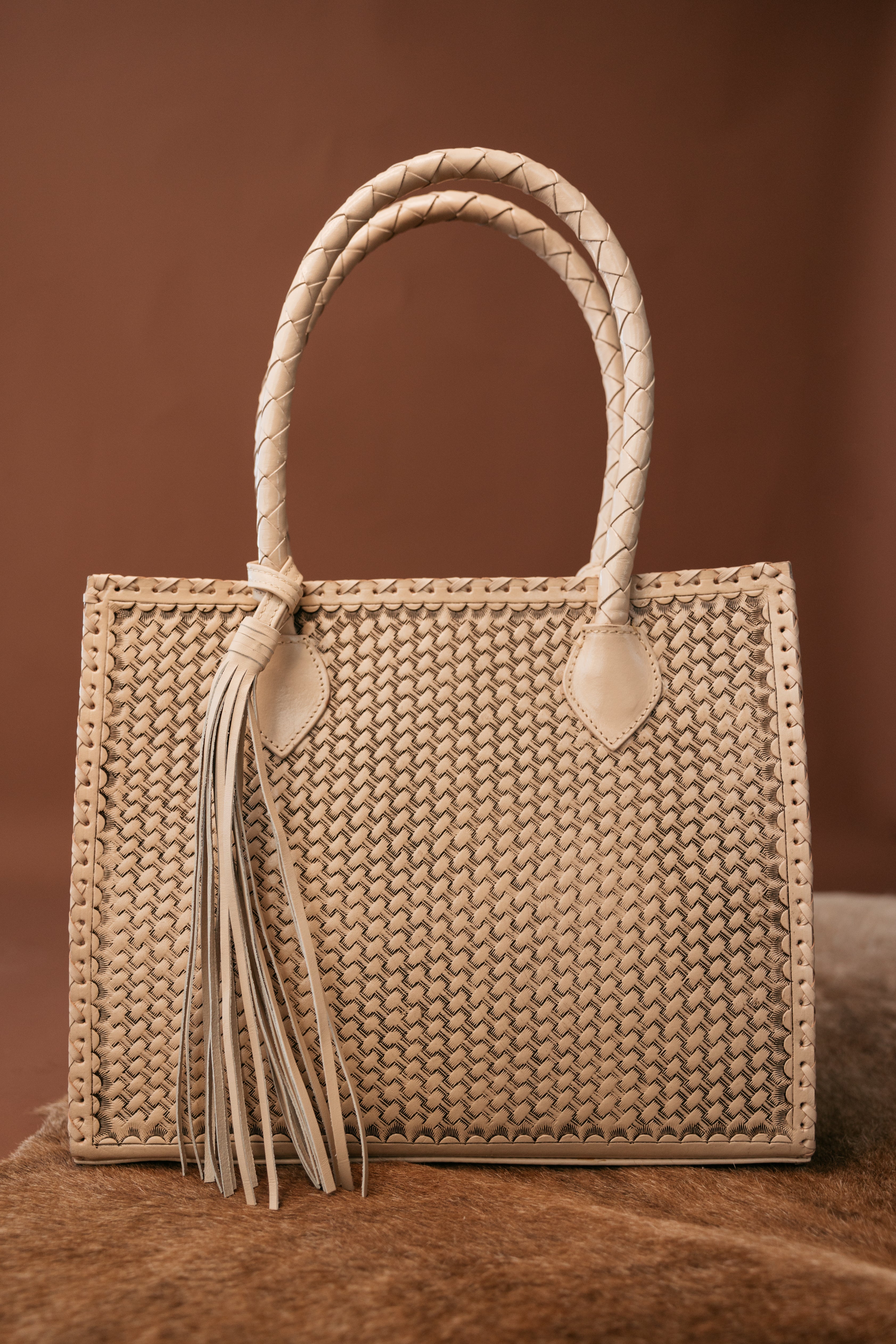 Woven leather western tote bag with braided handles and fringe tassel on brown background