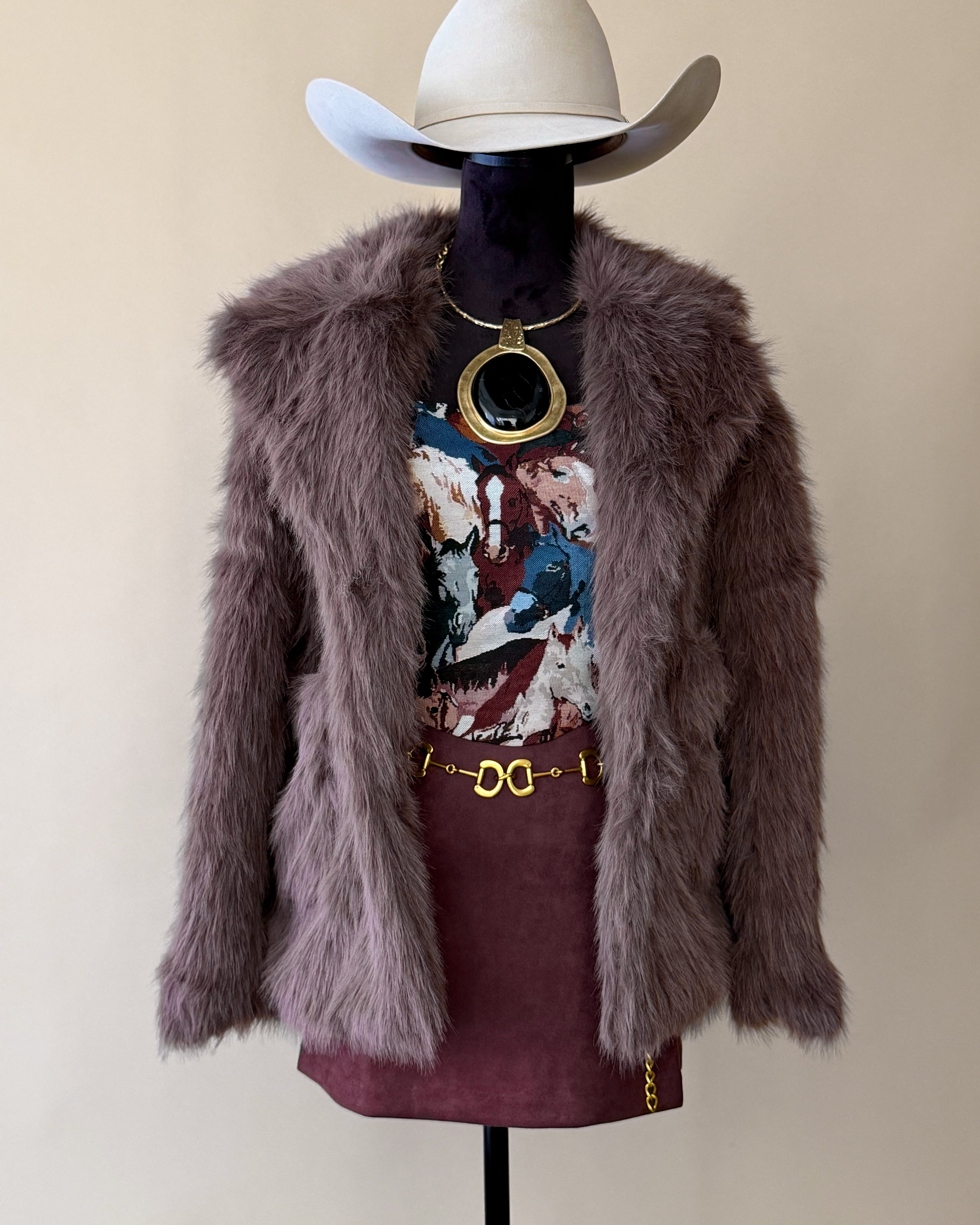 Western boho outfit with mauve faux fur jacket, cowboy hat, graphic tee, mini skirt, gold jewelry.