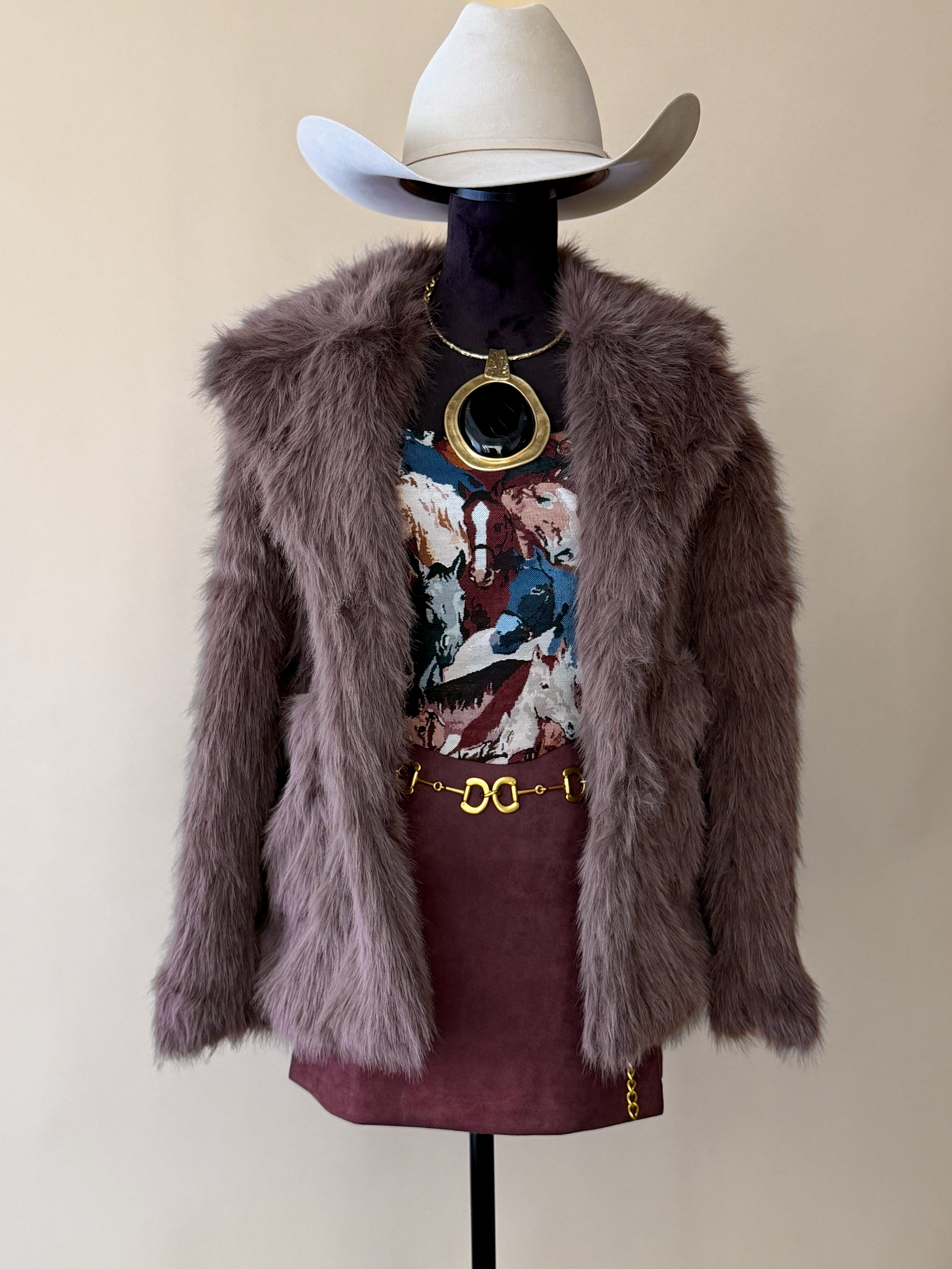 Western boho outfit with mauve faux fur jacket, cowboy hat, graphic tee, mini skirt, gold jewelry.