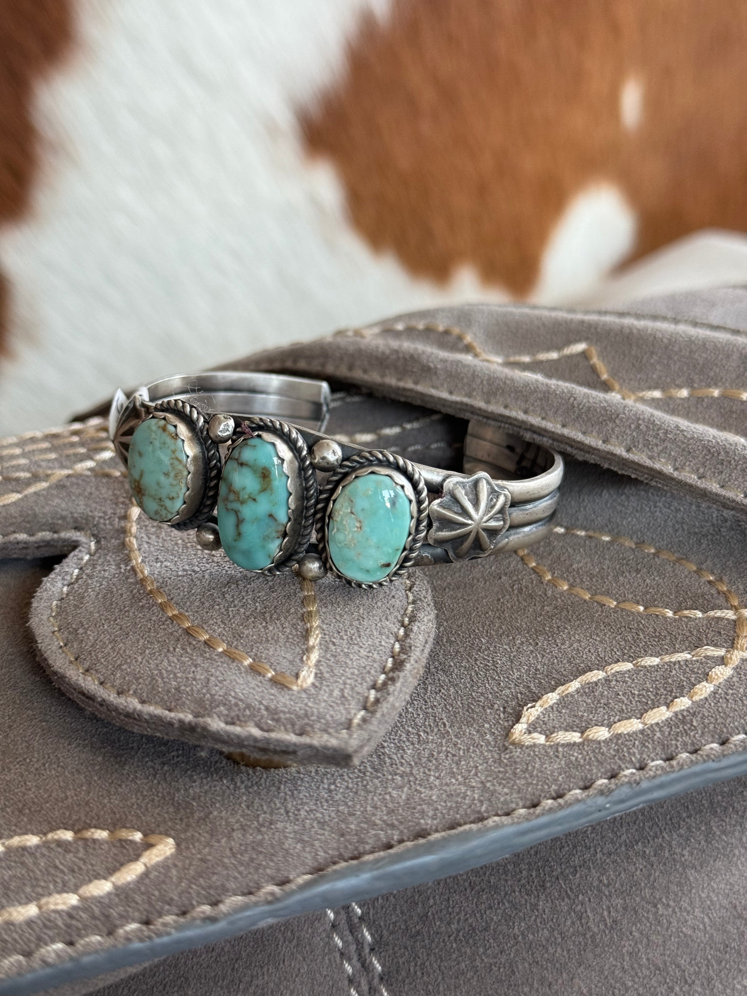 Silver cuff bracelet with three turquoise stones on embroidered suede, western style background.