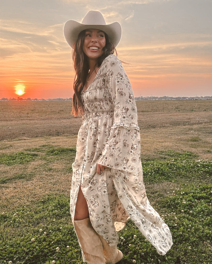 Woman in floral western dress, cowboy hat, and boots at sunset in a field