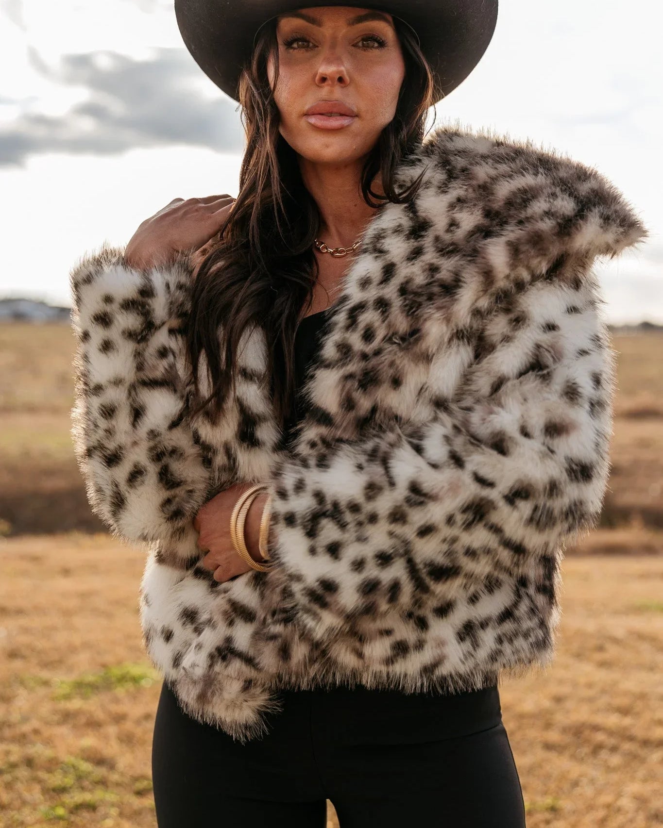 Woman in a western hat and leopard print faux fur jacket outdoors, boho cowgirl fashion
