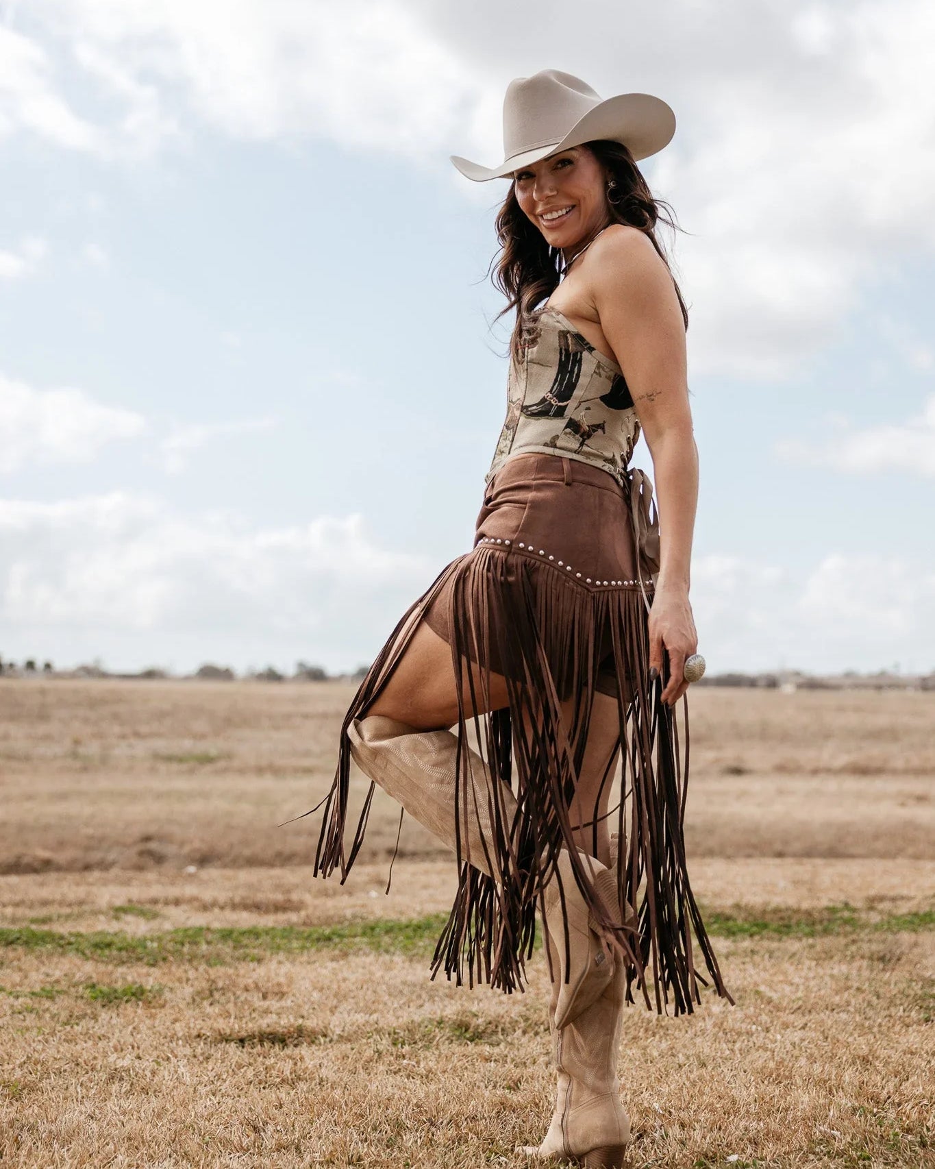 Woman in western cowgirl outfit with cowboy hat, fringe skirt, and boots standing outdoors