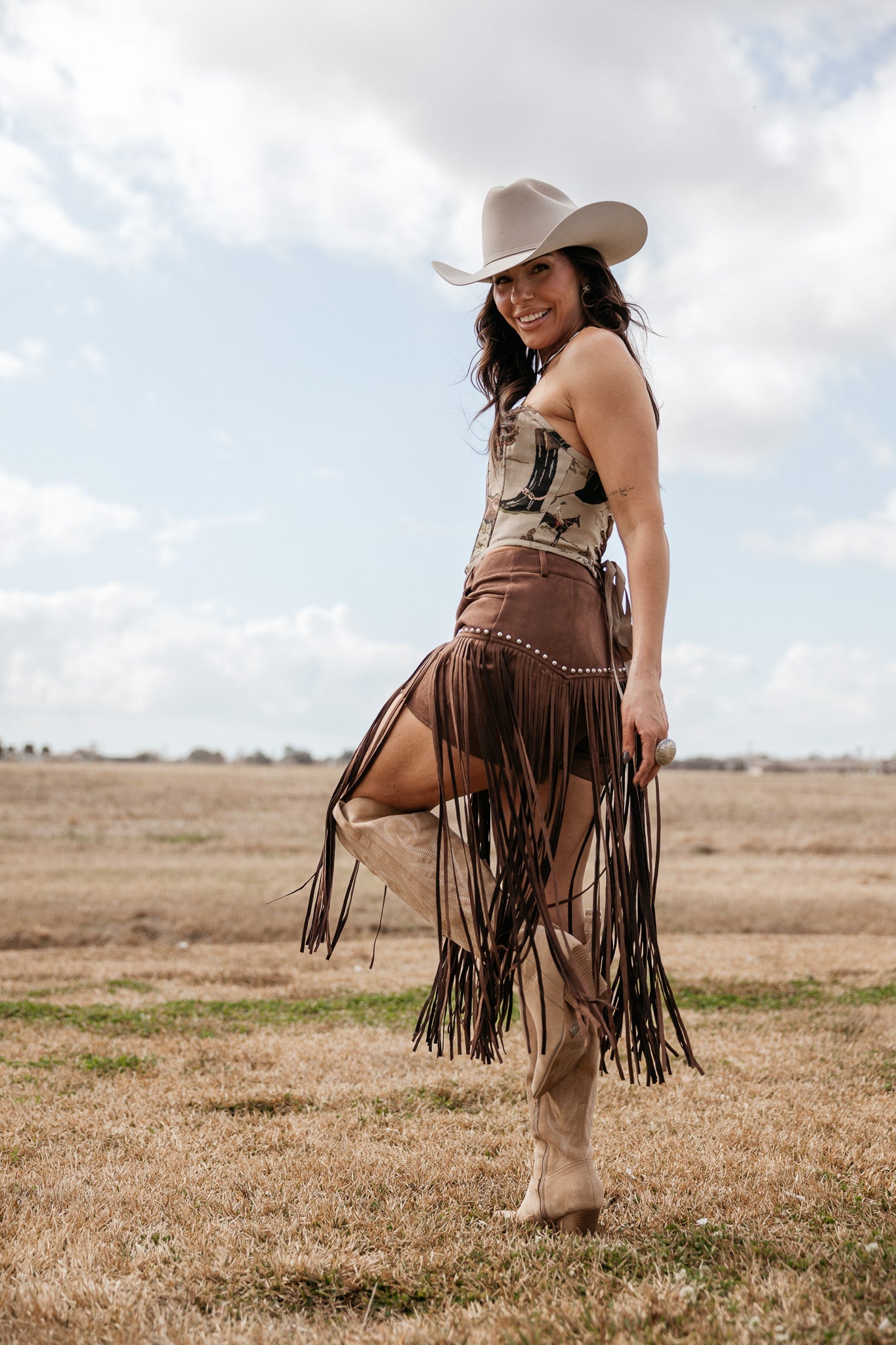 Woman in western cowgirl outfit with cowboy hat, fringe skirt, and boots standing outdoors
