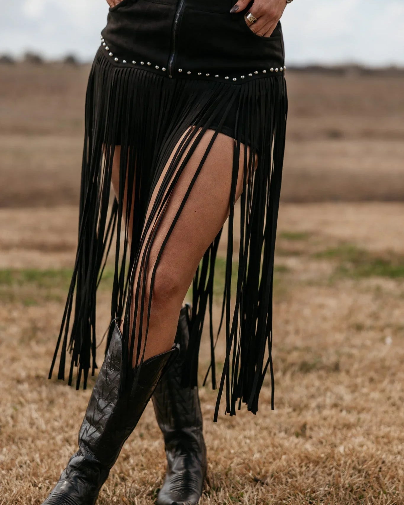 Woman wearing black fringe western skirt and cowboy boots in a rustic outdoor setting