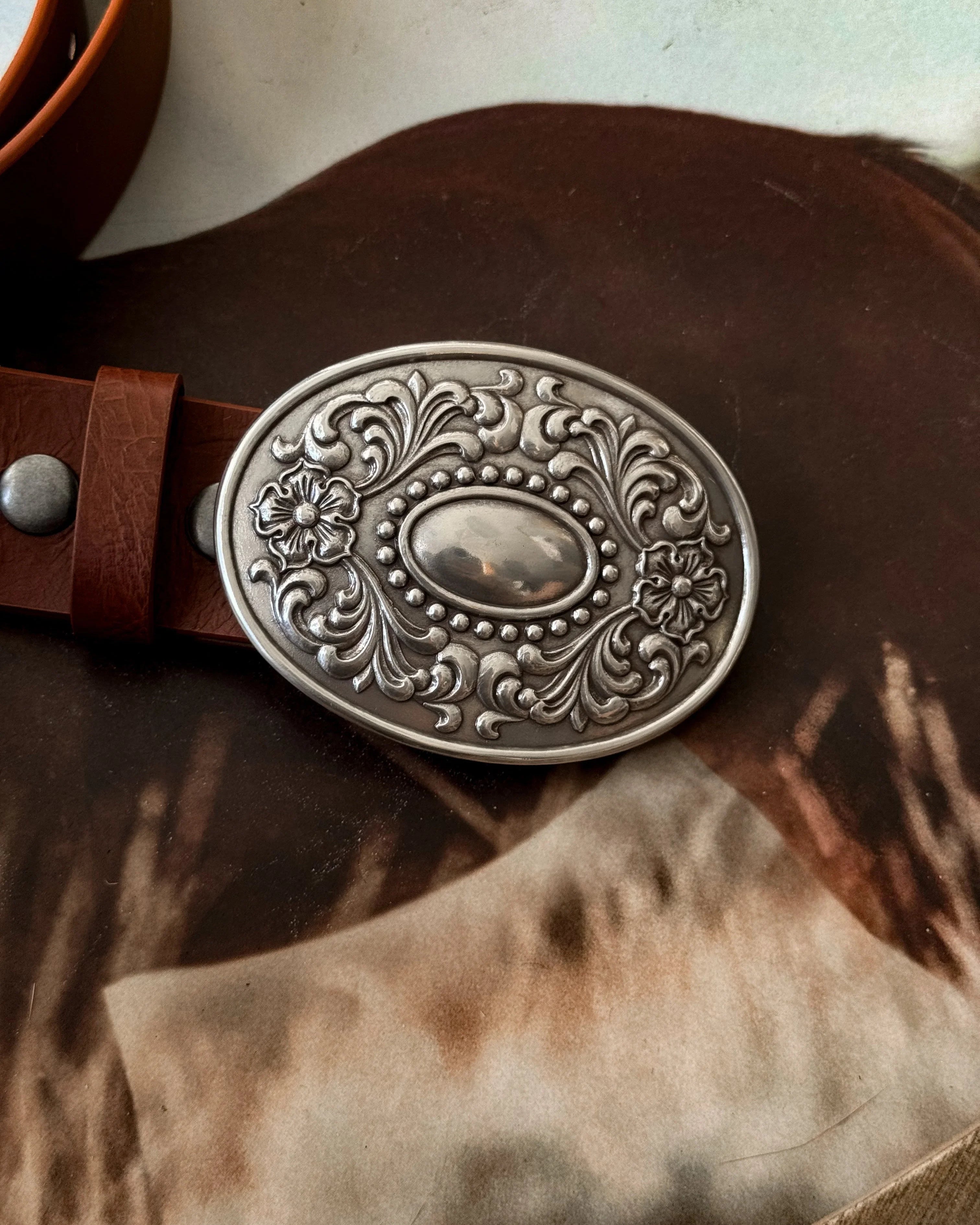 Western engraved silver belt buckle on brown leather strap, cowgirl accessory closeup