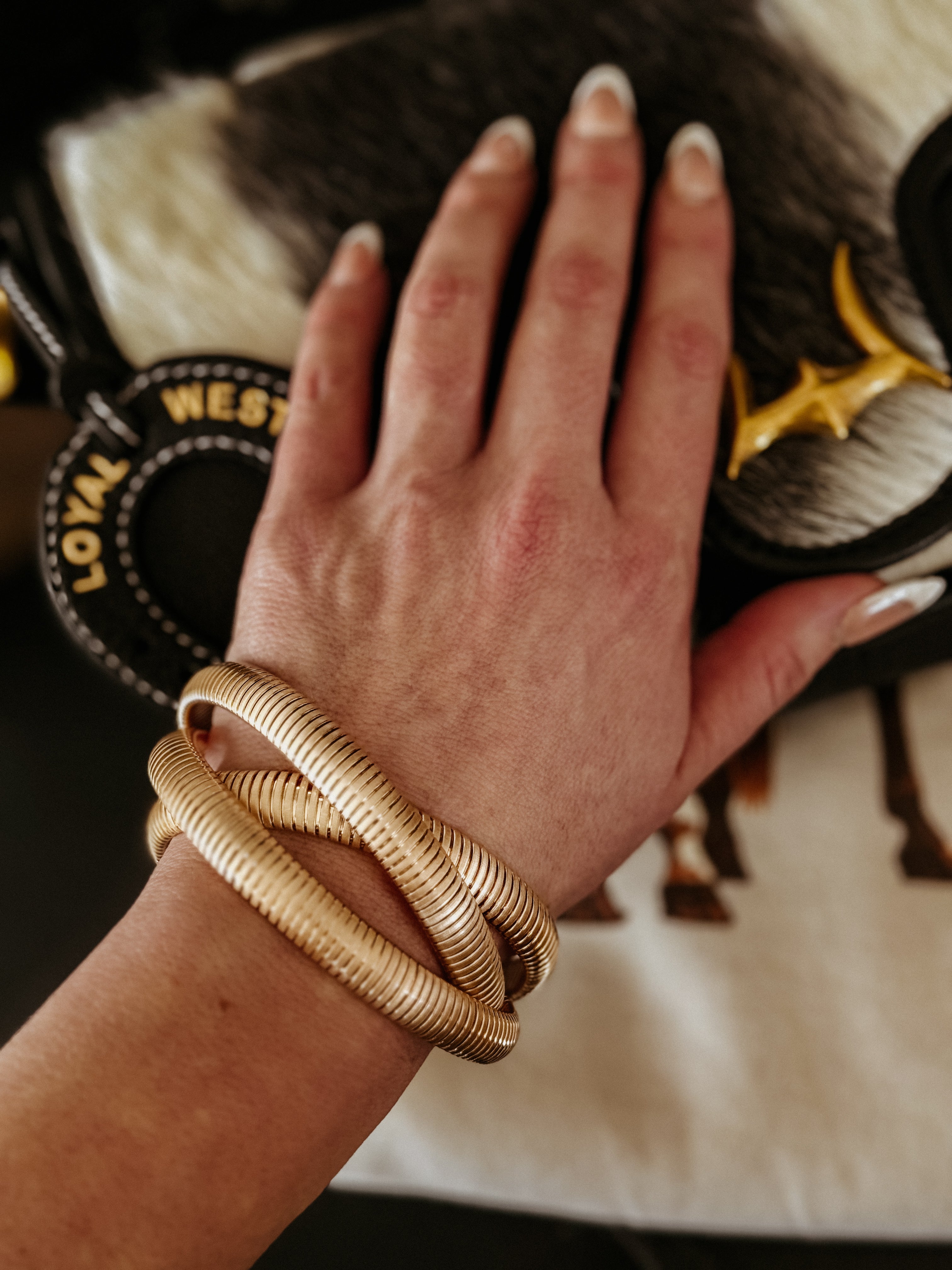 Woman wearing chunky gold western bracelets with cowhide purse in background