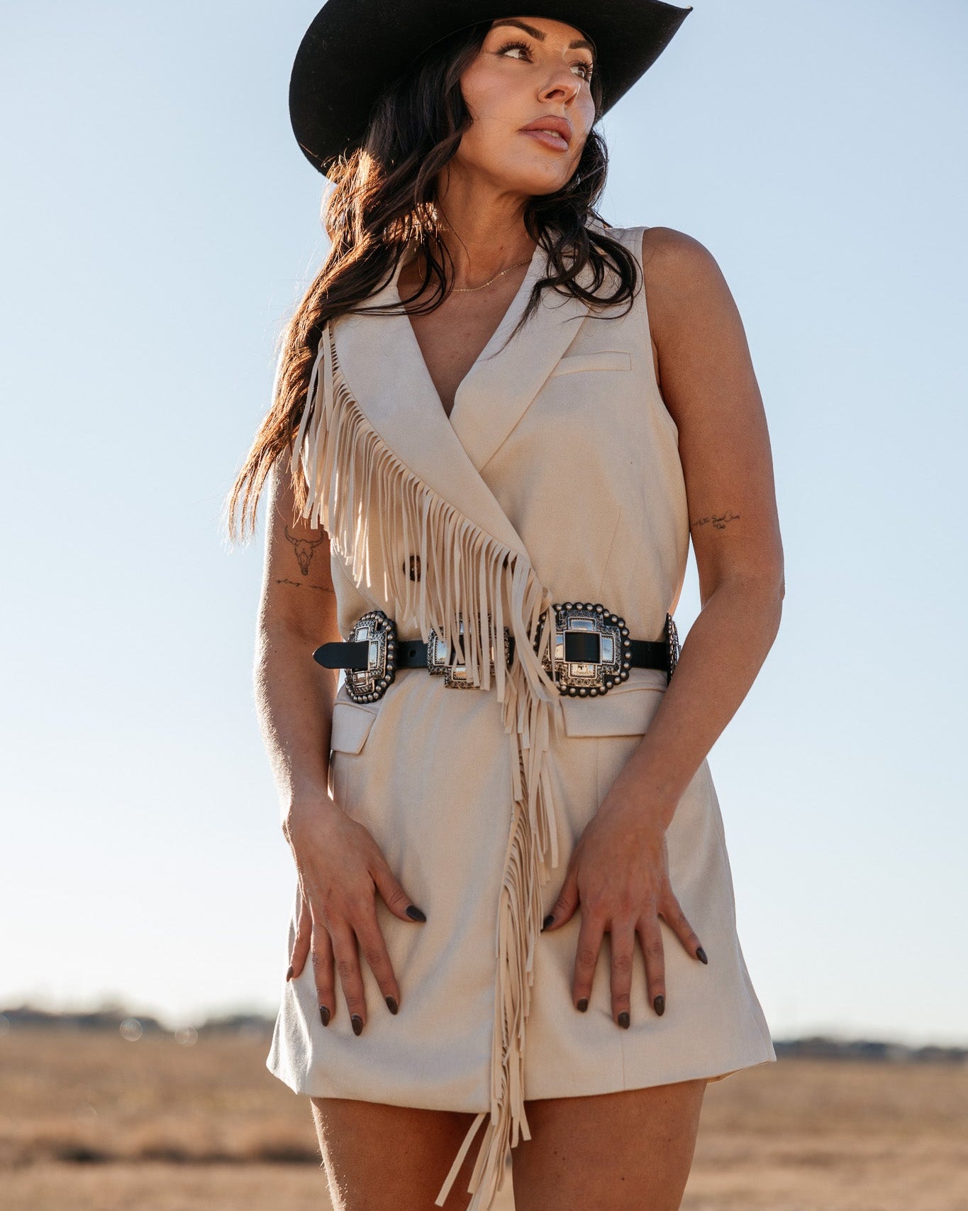 Woman in western fringe vest dress with concho belt and black cowboy hat in a field
