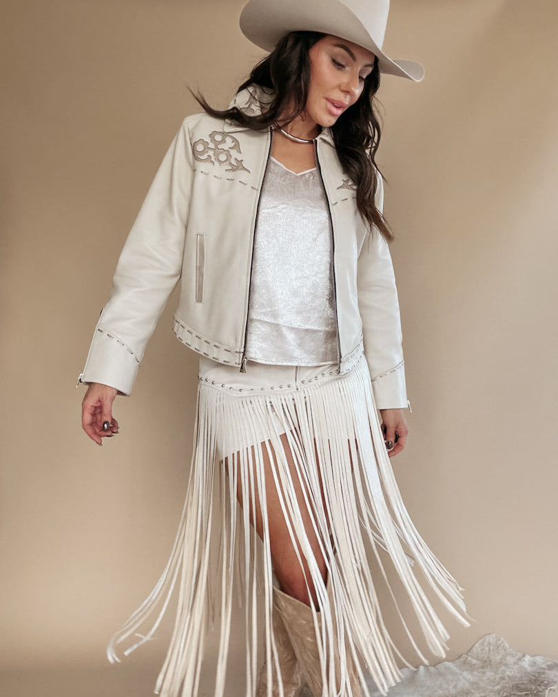 Woman in western boho outfit with white fringe skirt, embroidered jacket, cowboy hat and boots