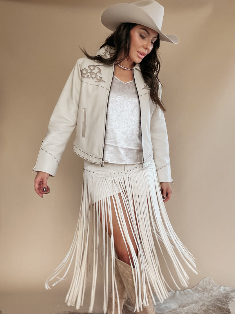 Woman in western boho outfit with white fringe skirt, embroidered jacket, cowboy hat and boots