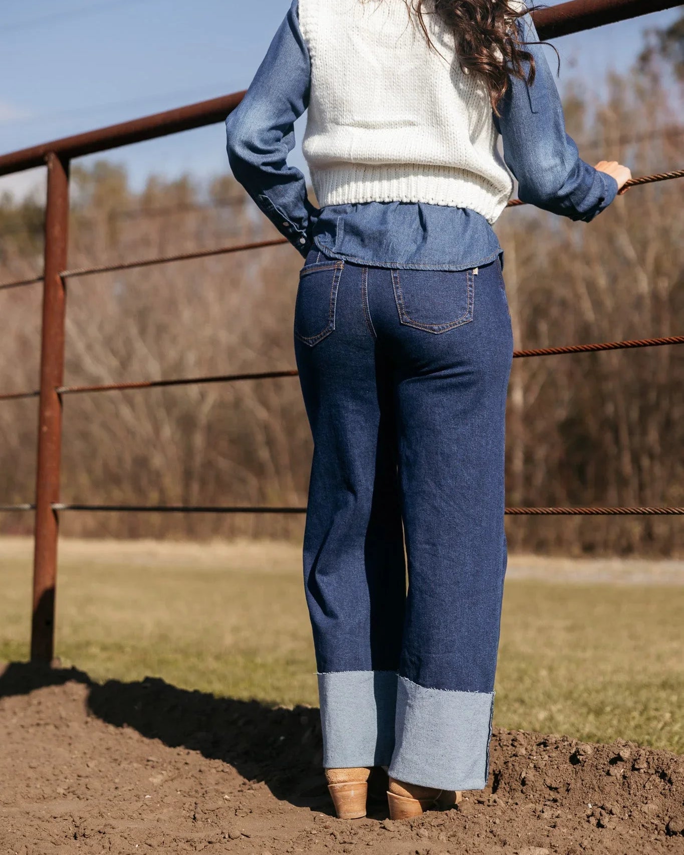 Woman in western boho outfit with wide leg denim jeans and white sweater vest outdoors