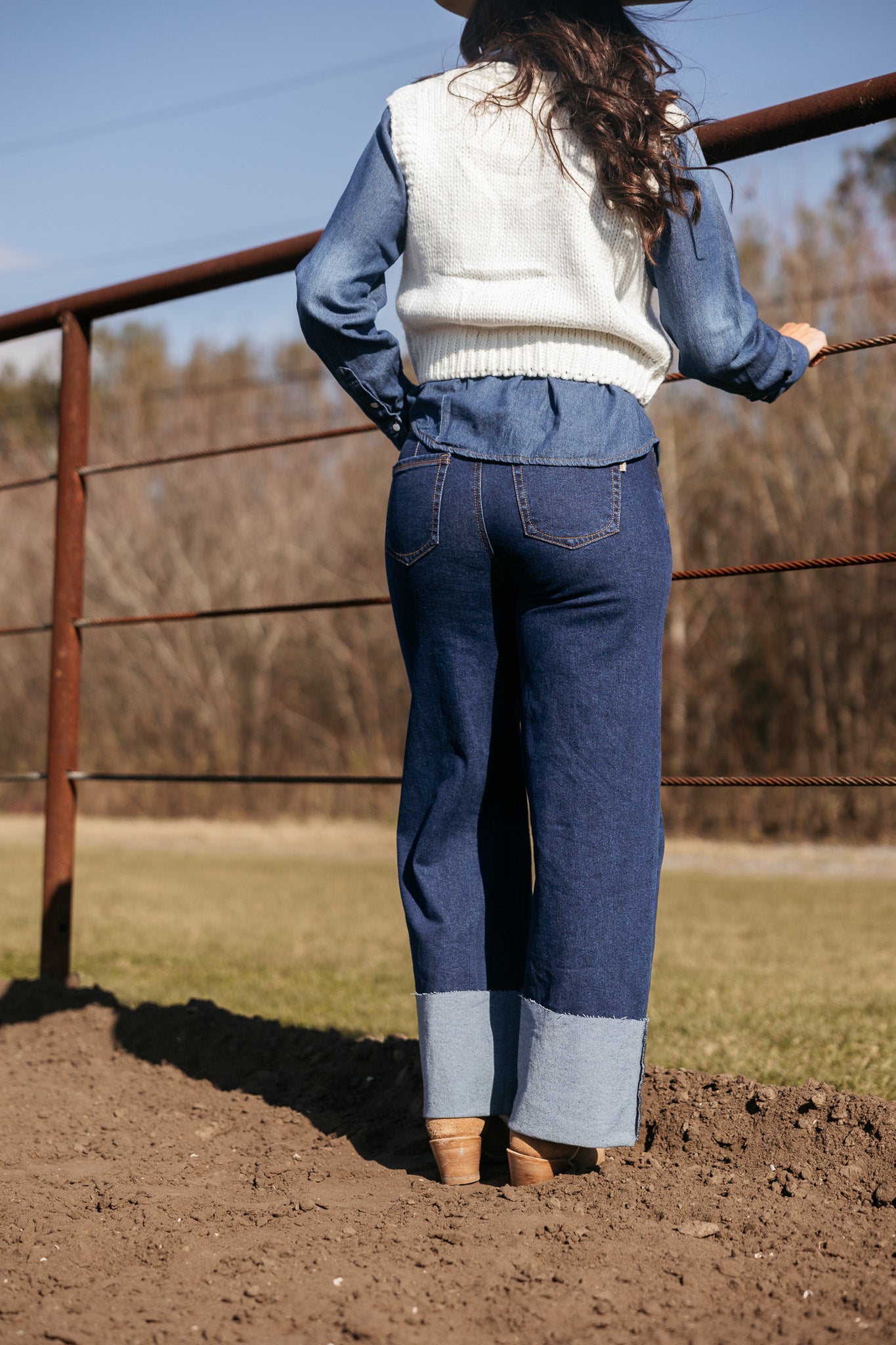 Woman in western boho outfit with wide leg denim jeans and white sweater vest outdoors