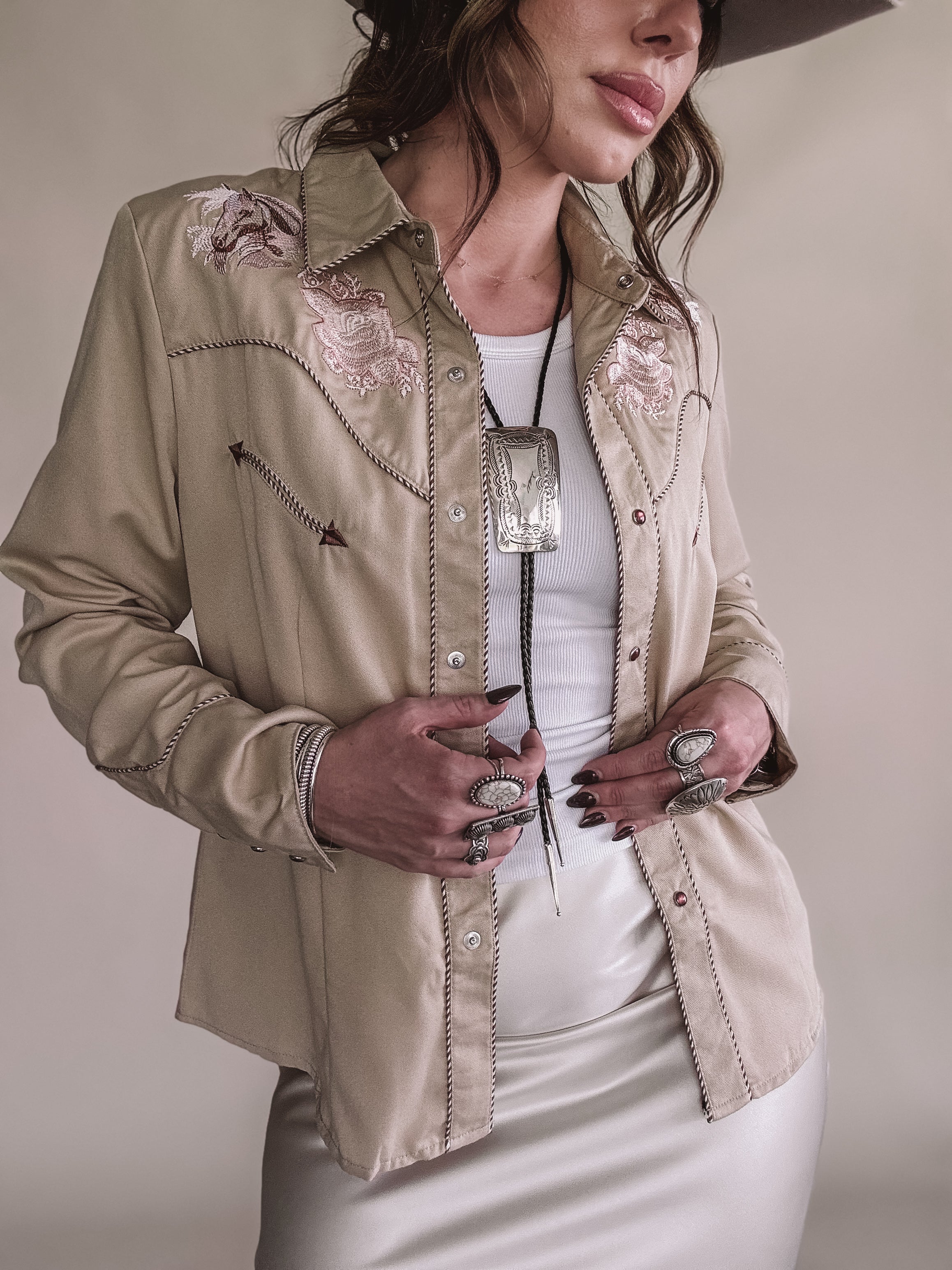 Woman in embroidered western shirt, white tank, bolo tie, and silver western jewelry