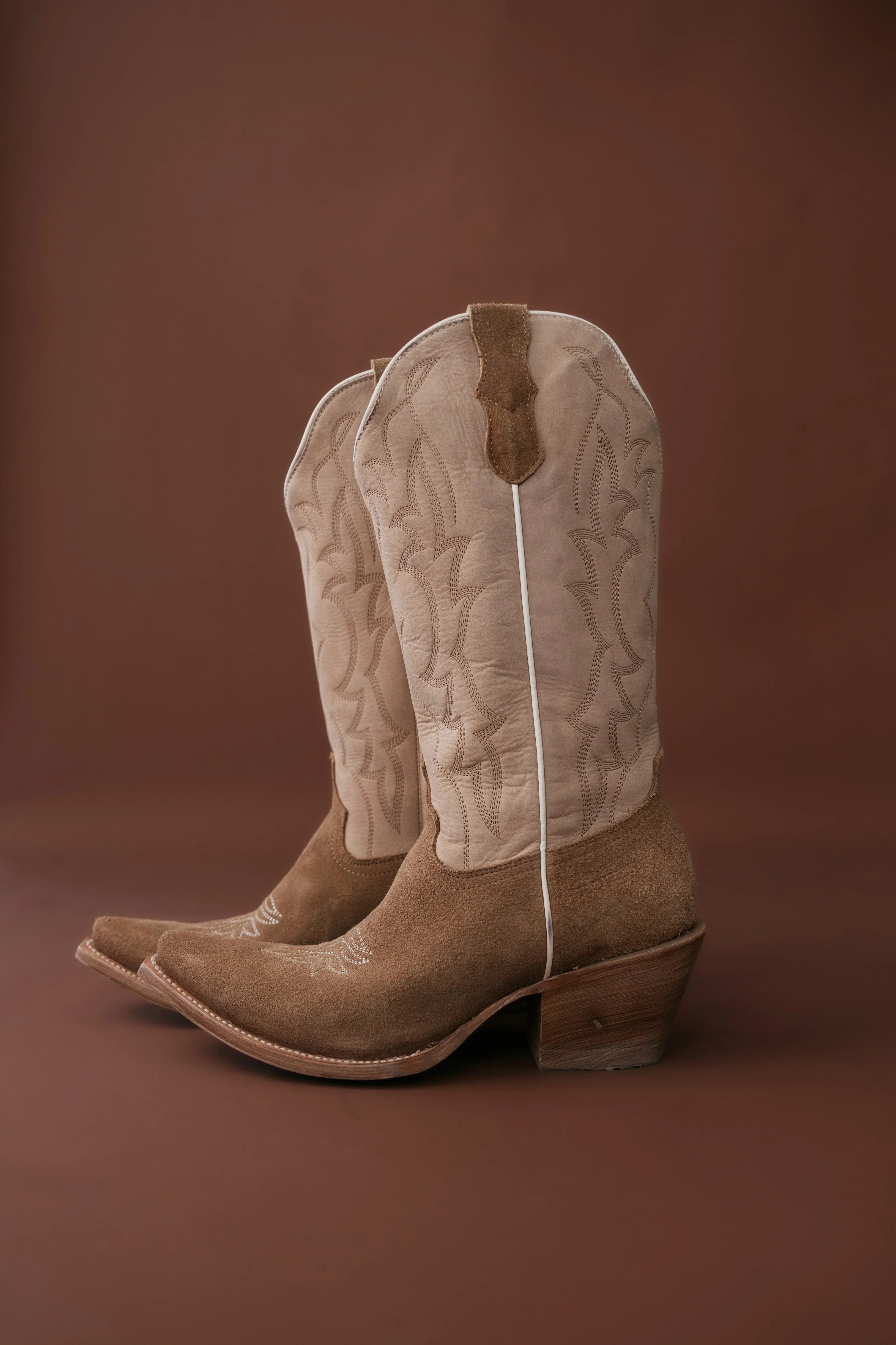 Pair of beige cowboy boots with white laces on a brown background