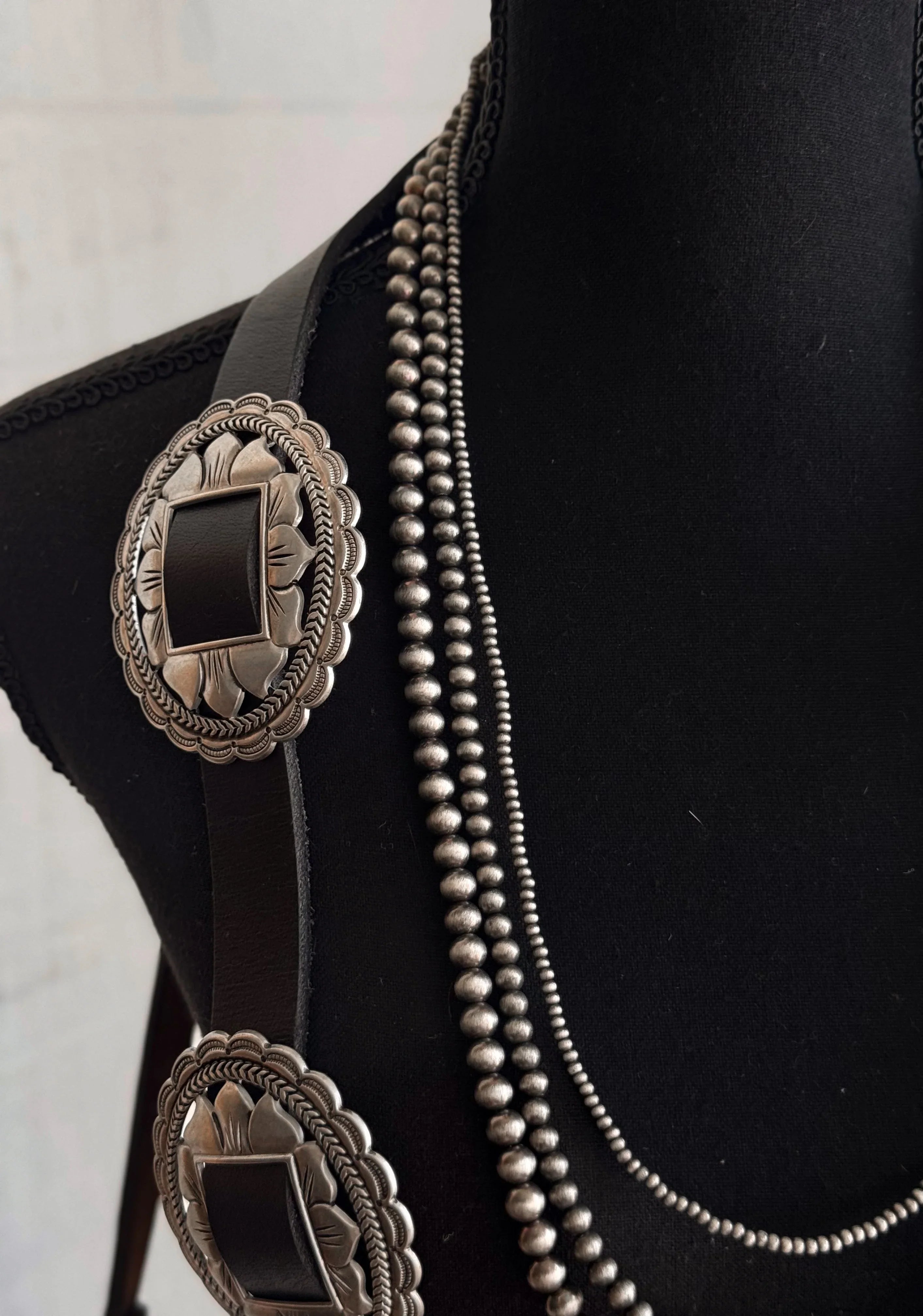 Close-up of a black boot with silver concho belt and necklace on a white background