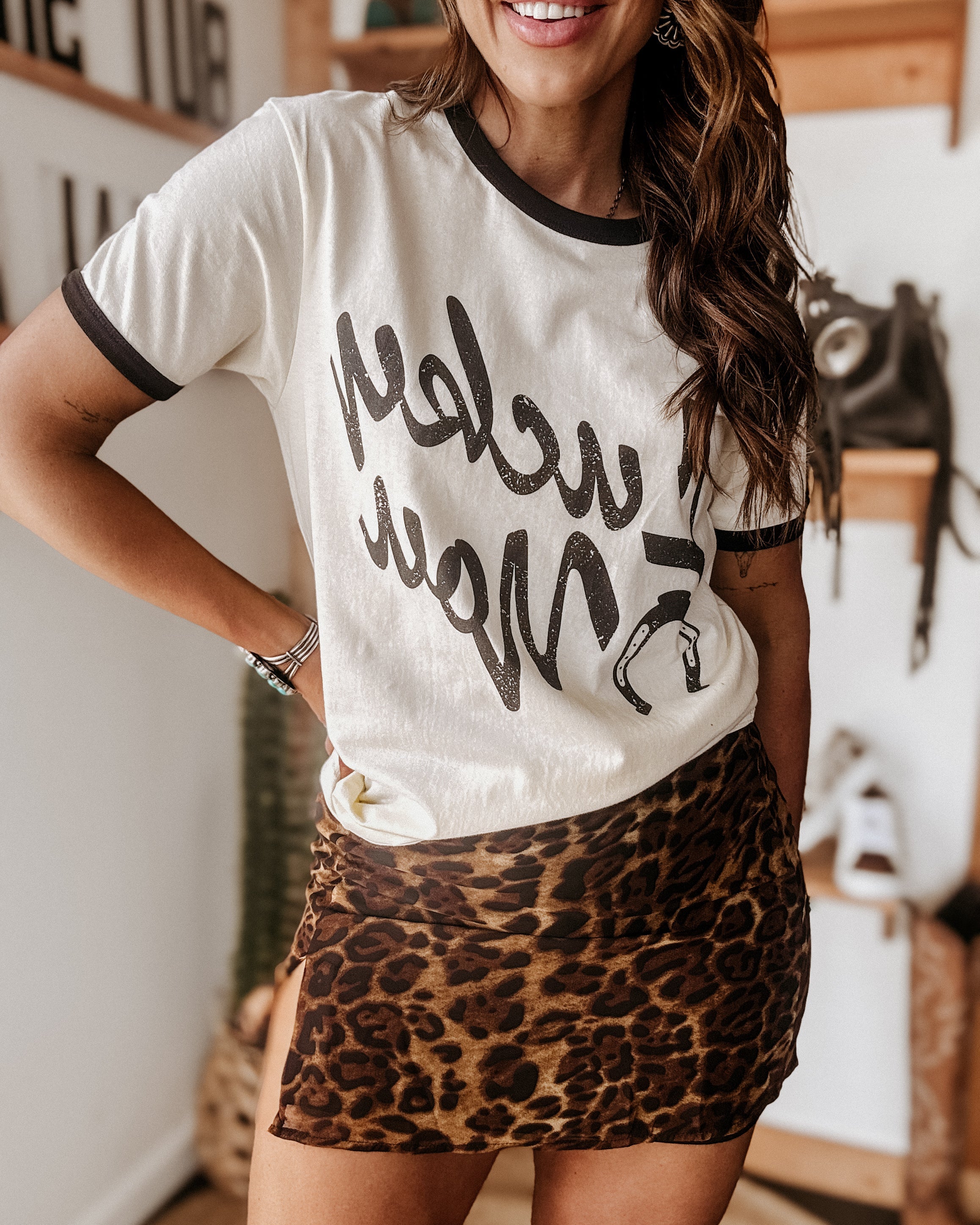 Woman in western graphic tee and leopard print mini skirt in boho boutique setting