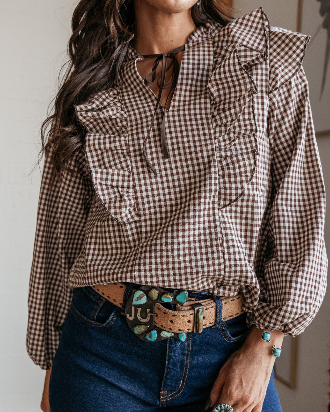 Woman in brown gingham ruffle blouse, turquoise western belt, and denim jeans