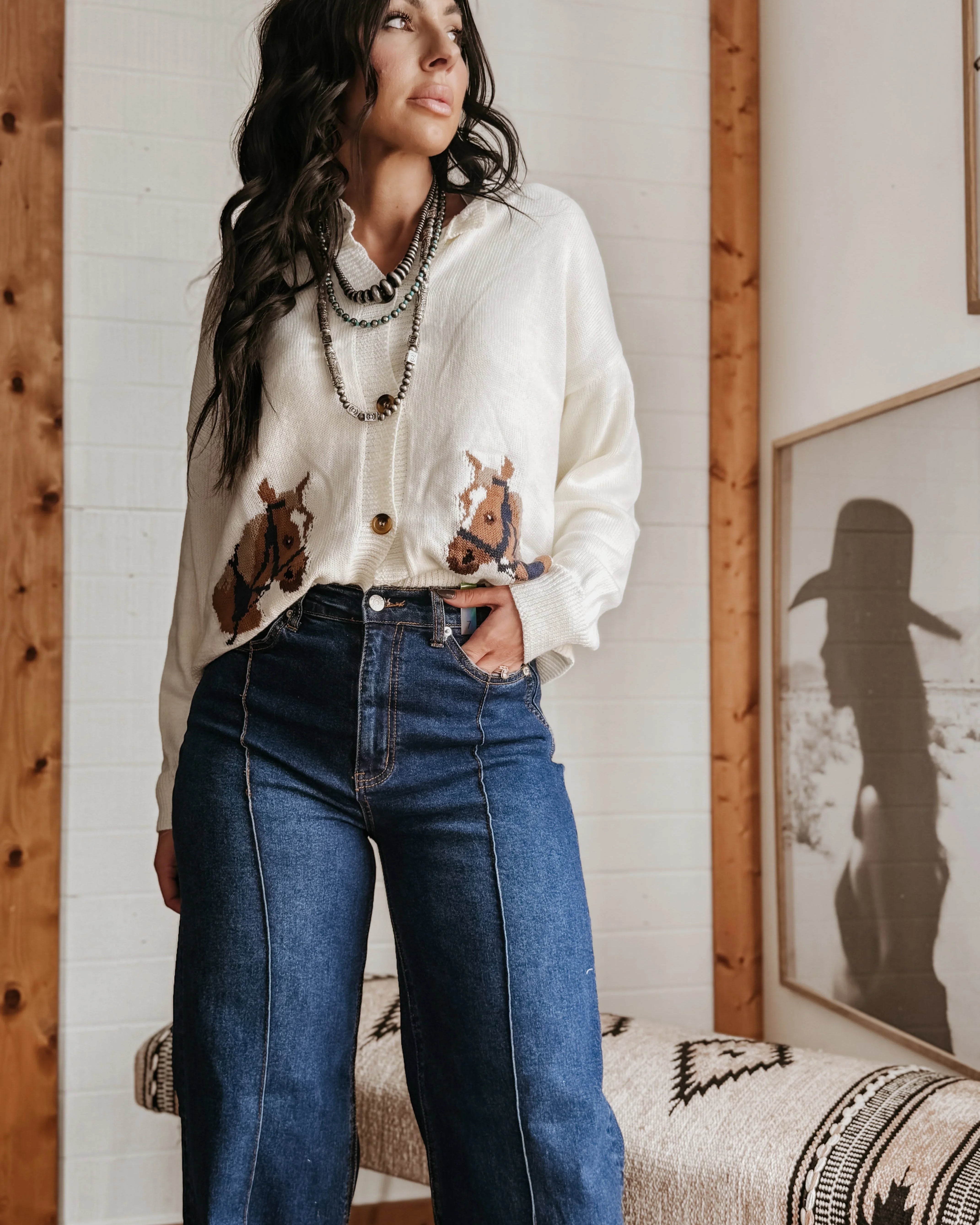 Woman in a western boho outfit with cow print cardigan, layered necklaces, and wide-leg jeans