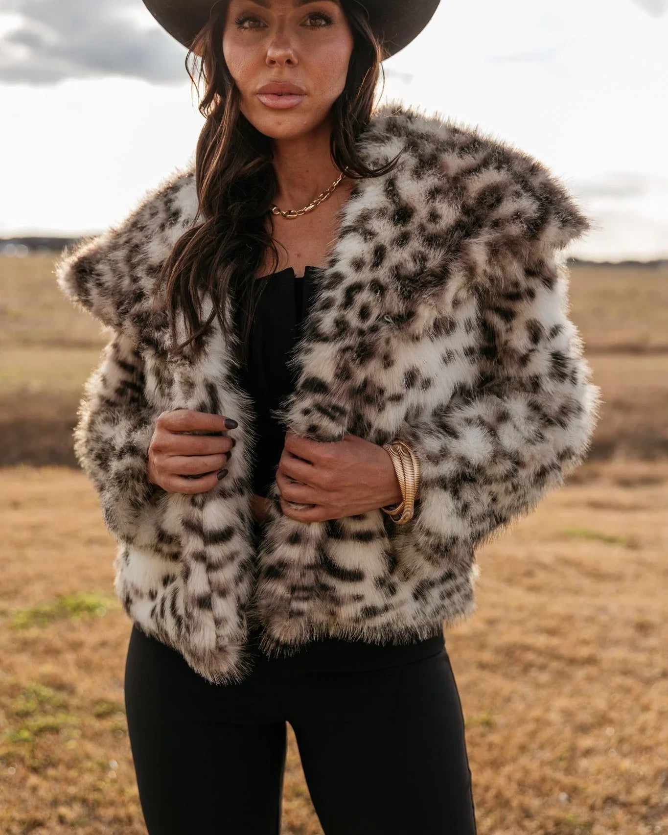 Woman in a black cowboy hat and faux fur leopard print jacket, western boho style outfit outdoors