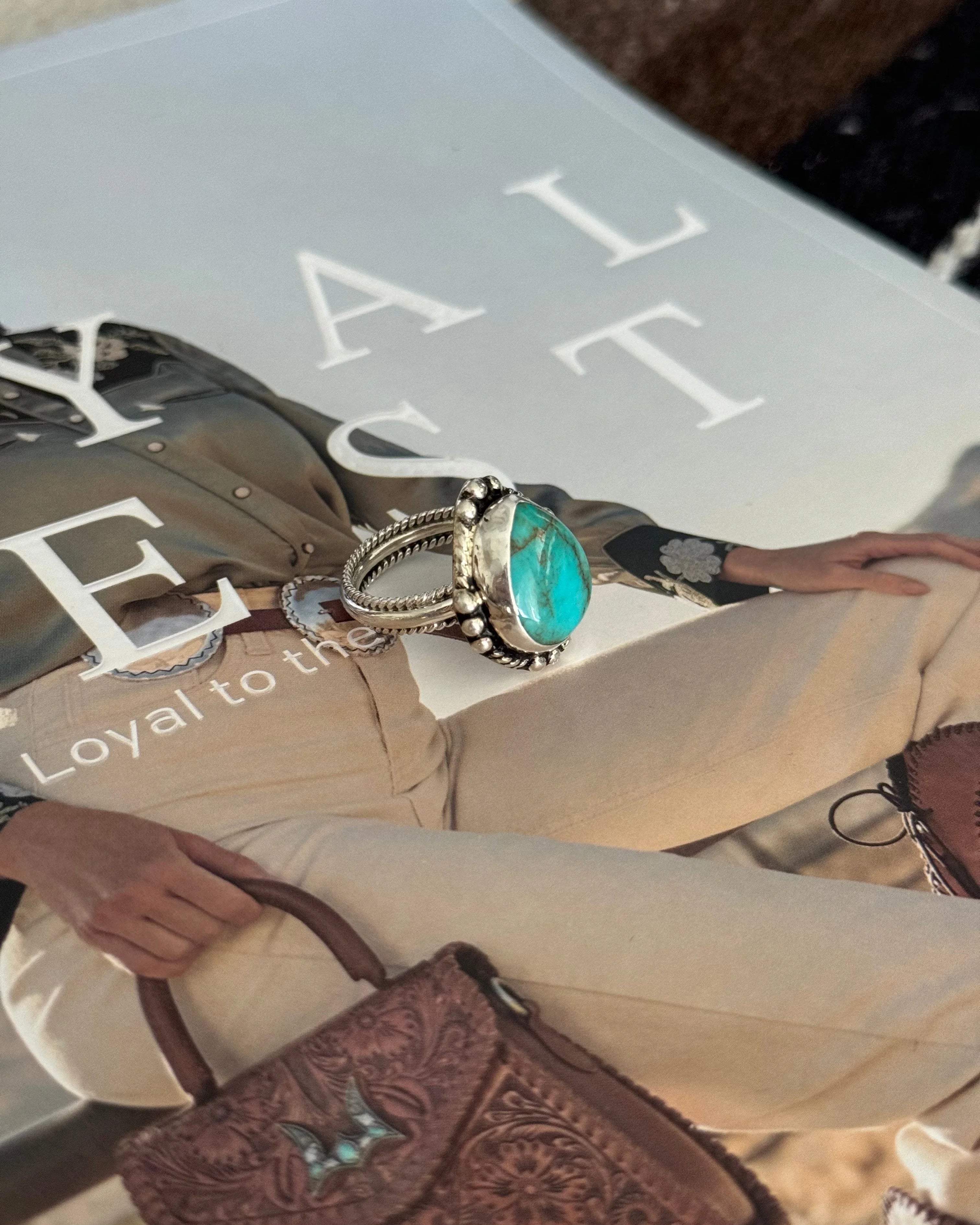 Turquoise western silver ring on cowgirl fashion magazine with tooled leather handbag.