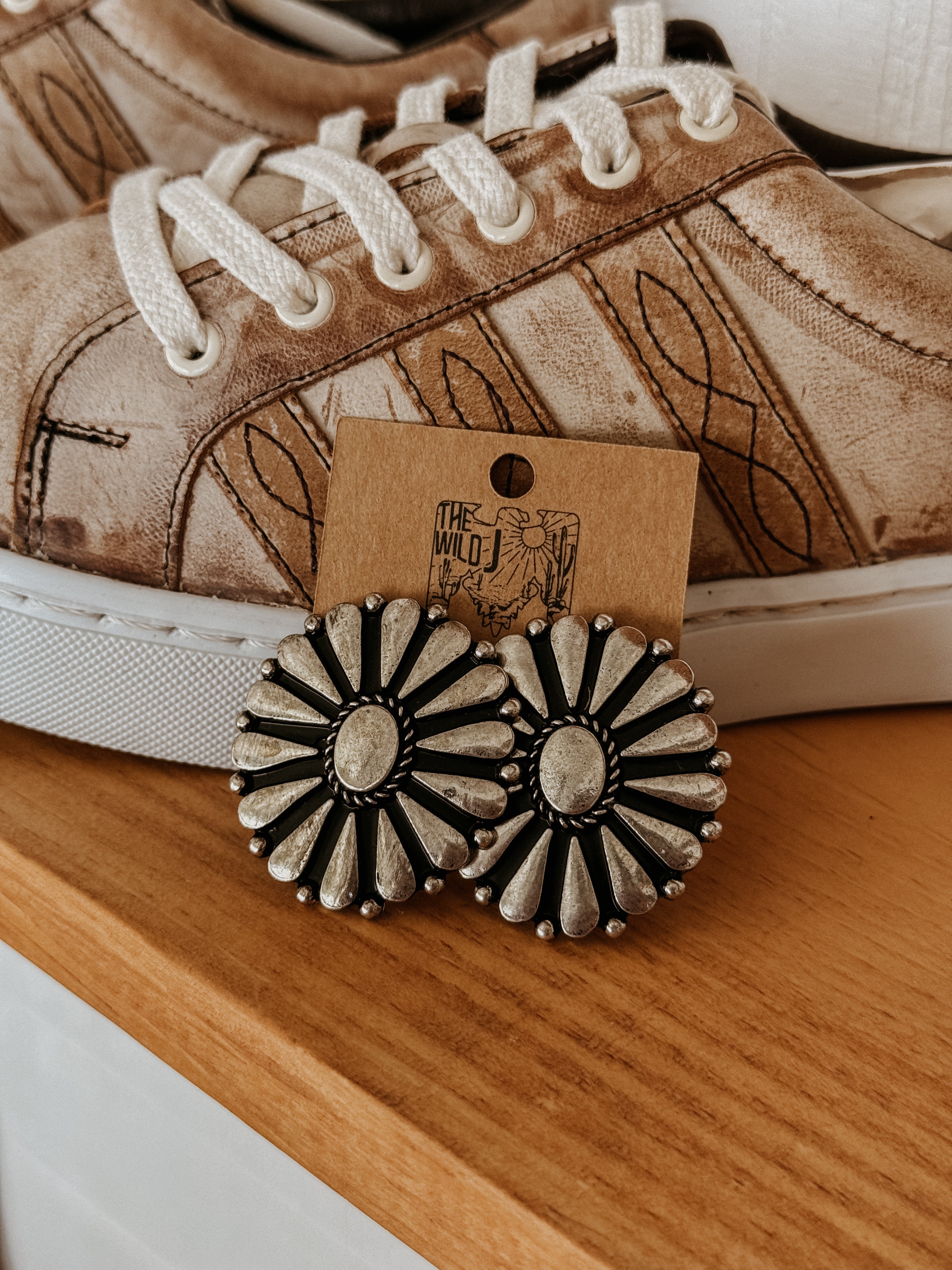 Western concho statement earrings with silver floral design displayed near boho sneakers