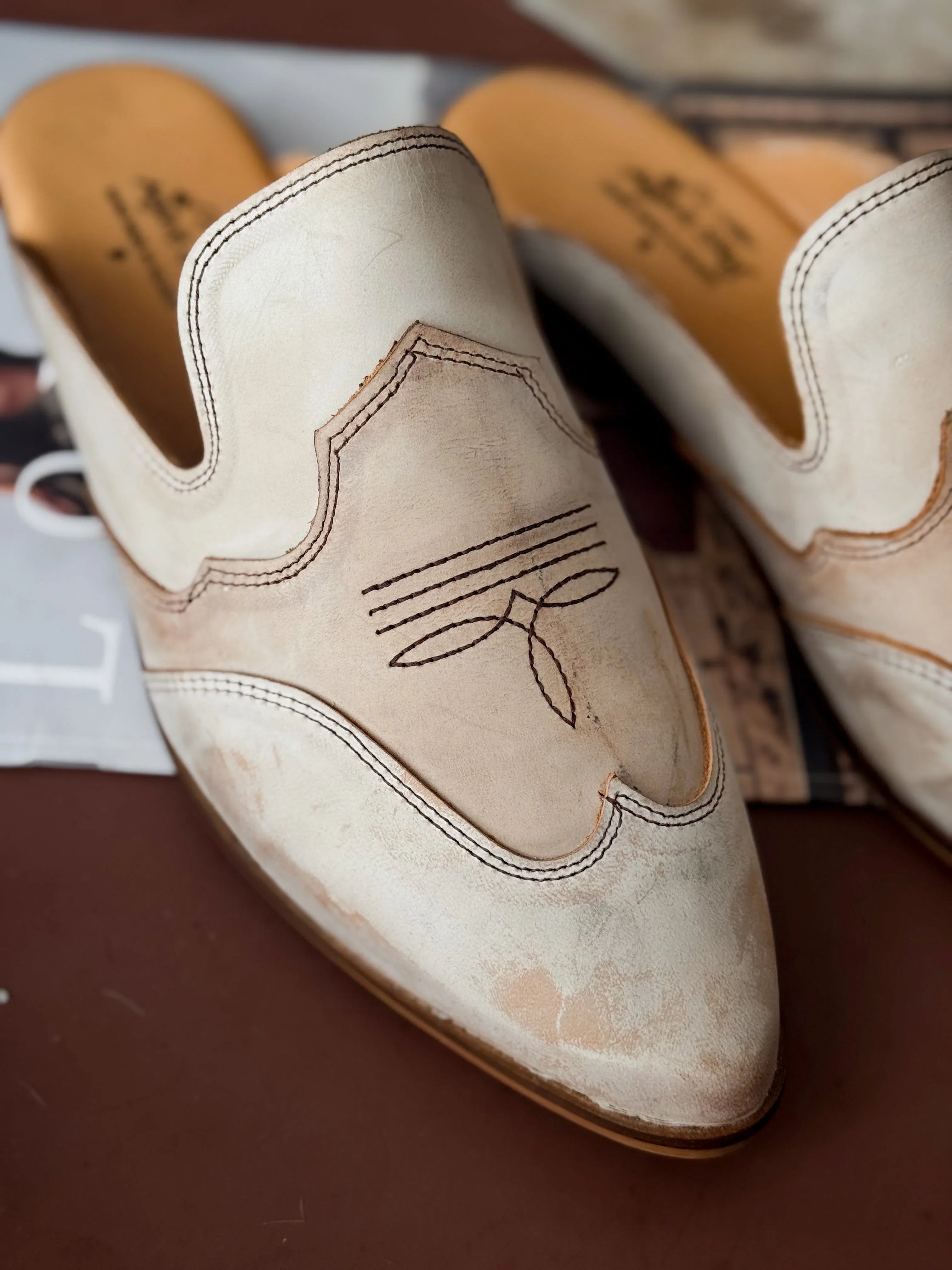 Pair of beige leather shoes with intricate stitching on a brown surface