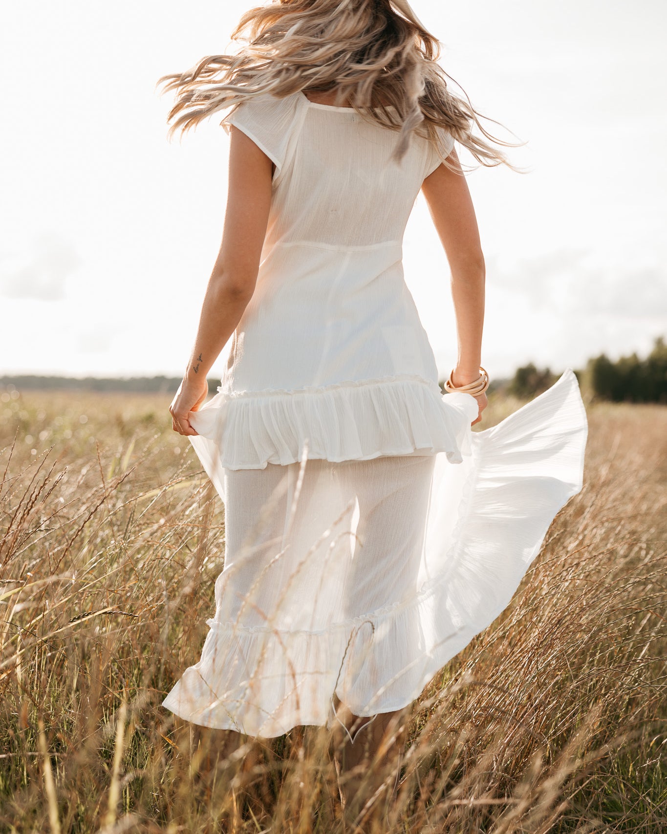 Woman in a white dress and hat standing in a field of tall grass.