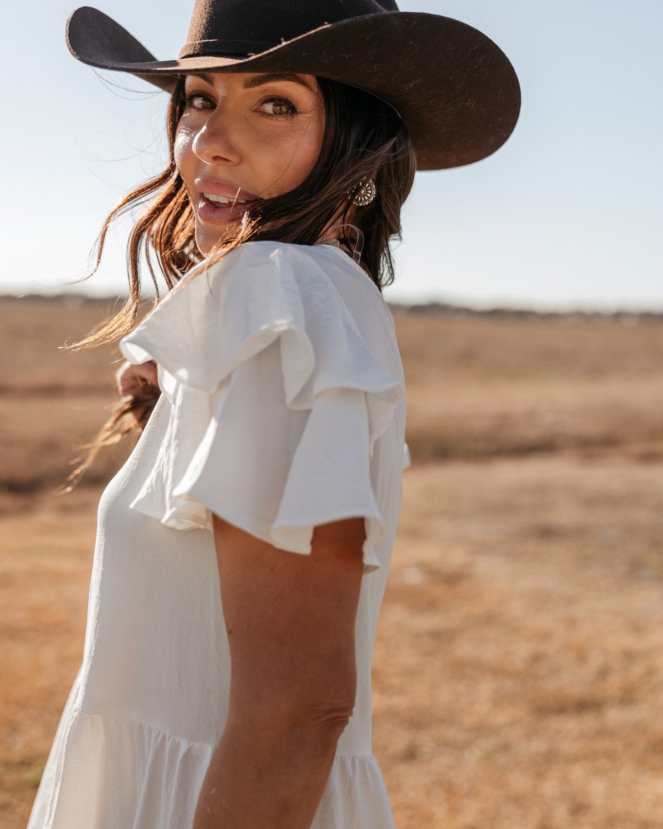 Woman in brown cowboy hat and white ruffle western dress in sunny outdoor field