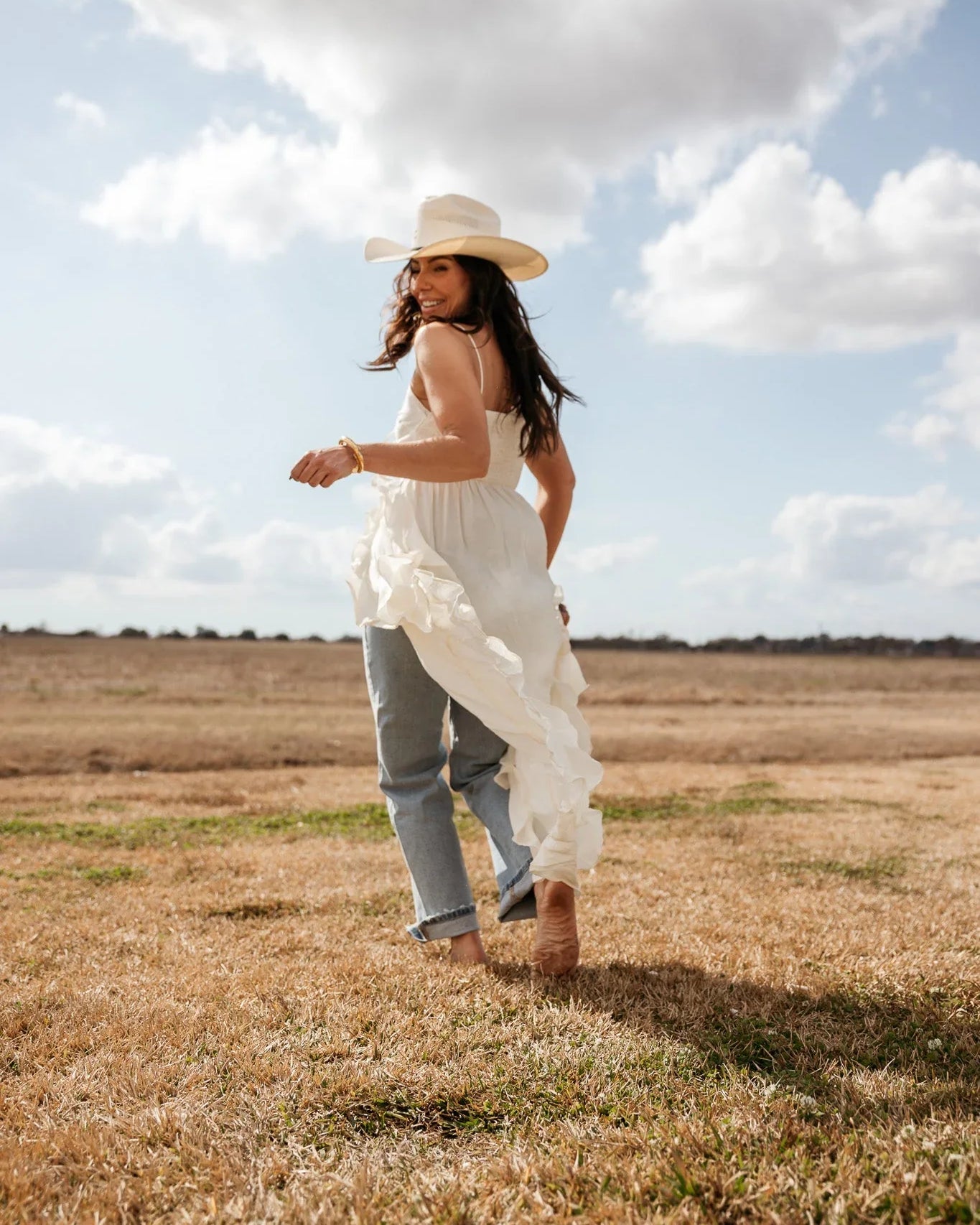 Woman in a white cowboy hat, ruffled boho dress, and jeans in a western field