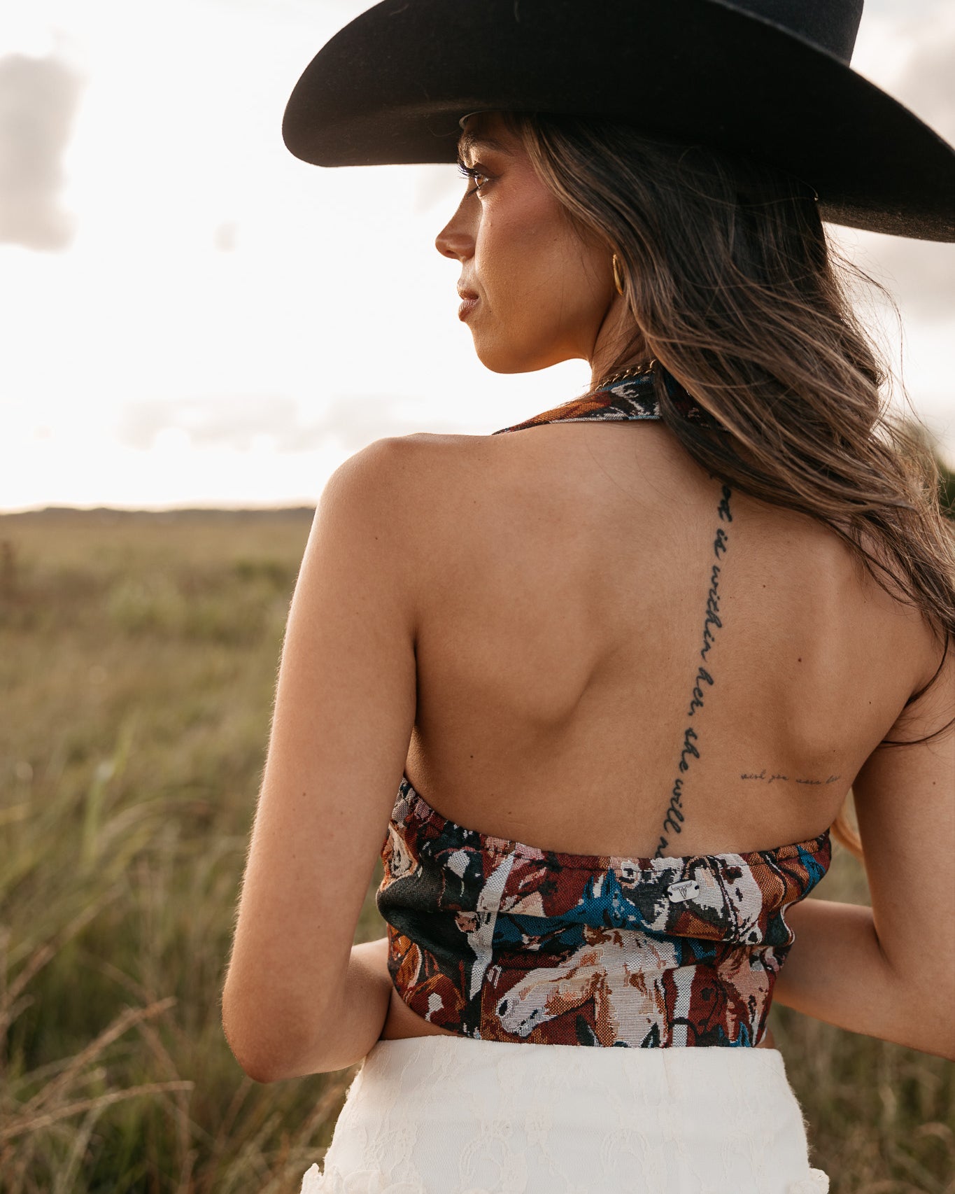 women wearing horse pattern halter top with low back and a white skirt standing in a field.