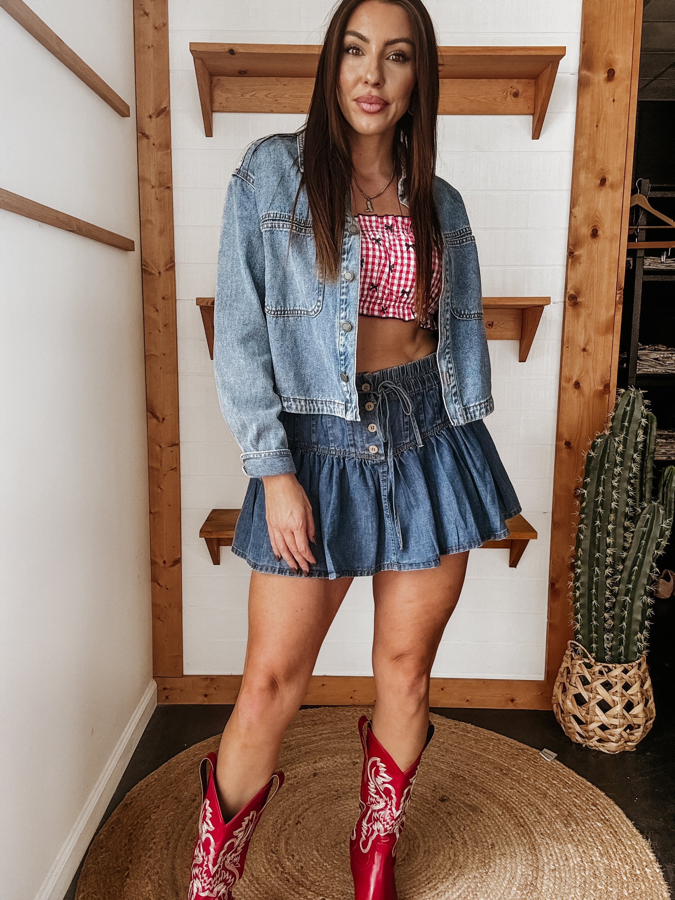 Woman in a denim jacket and skirt, red cowgirl boots, and gingham crop top, western boho style