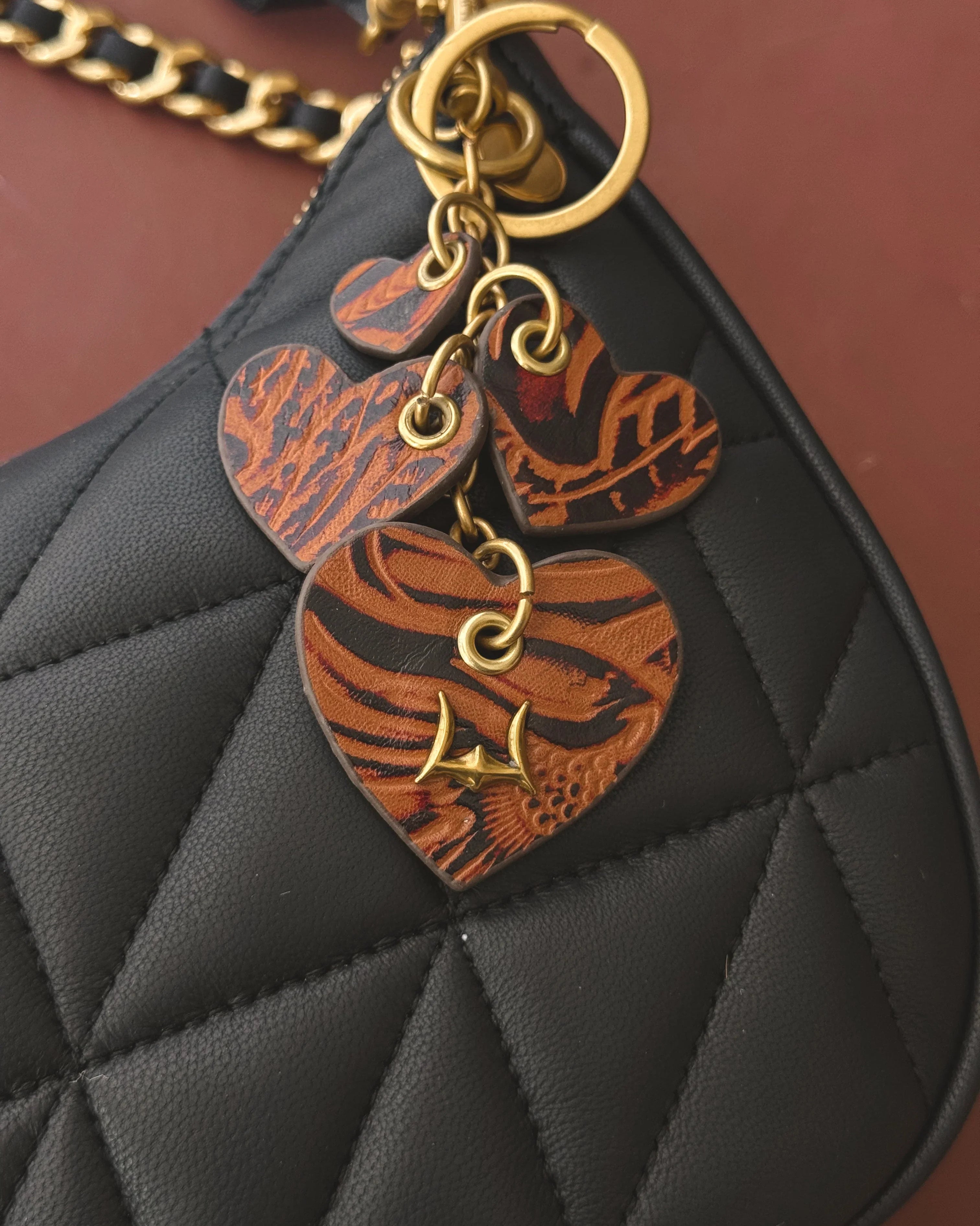 Black quilted handbag with heart-shaped leather charms on a brown background