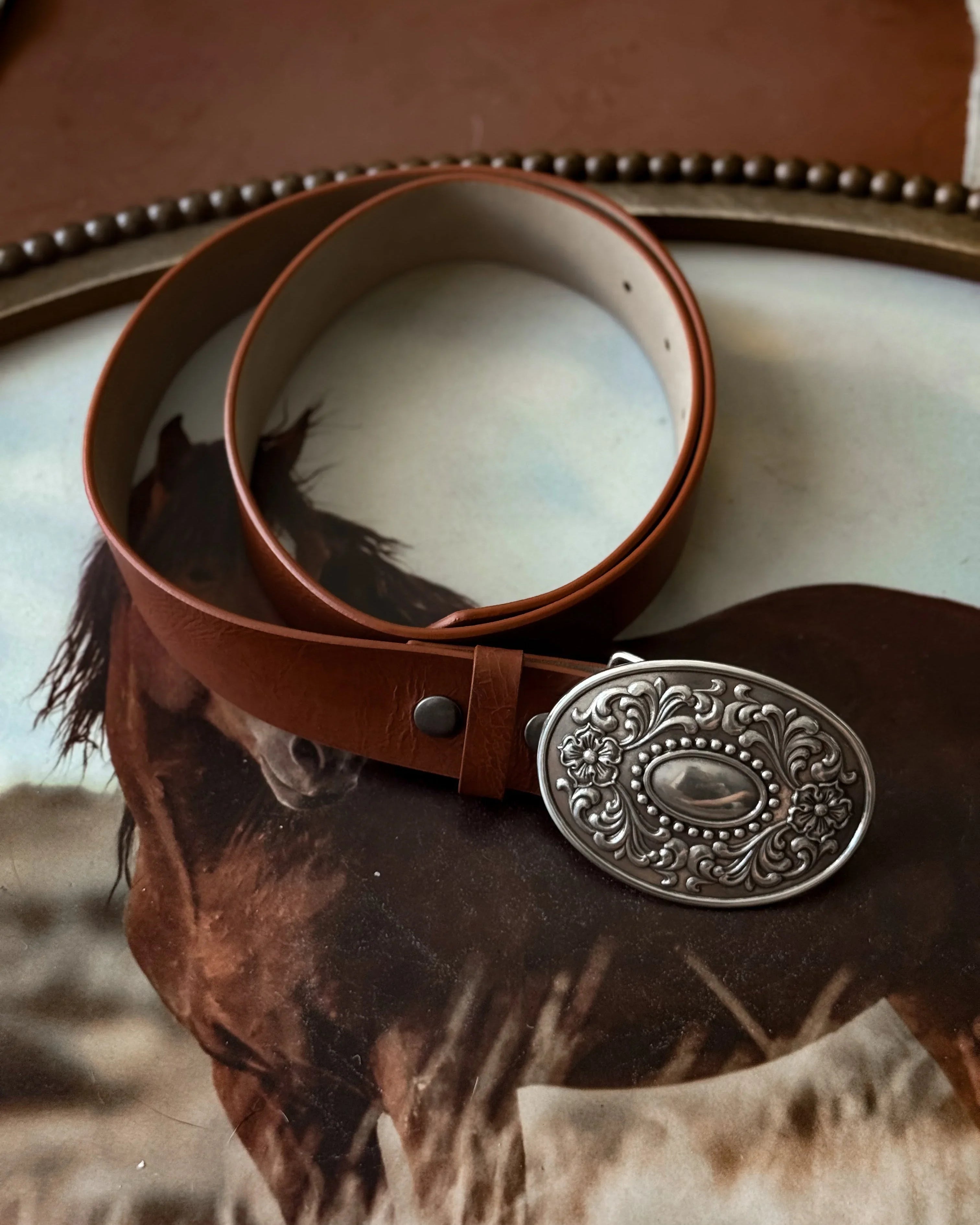 Brown western belt with ornate silver buckle on horse background, cowgirl fashion accessory