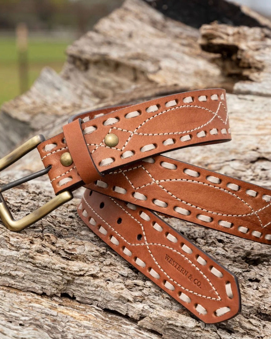 Brown tooled leather western belt with brass buckle and white stitching on wood