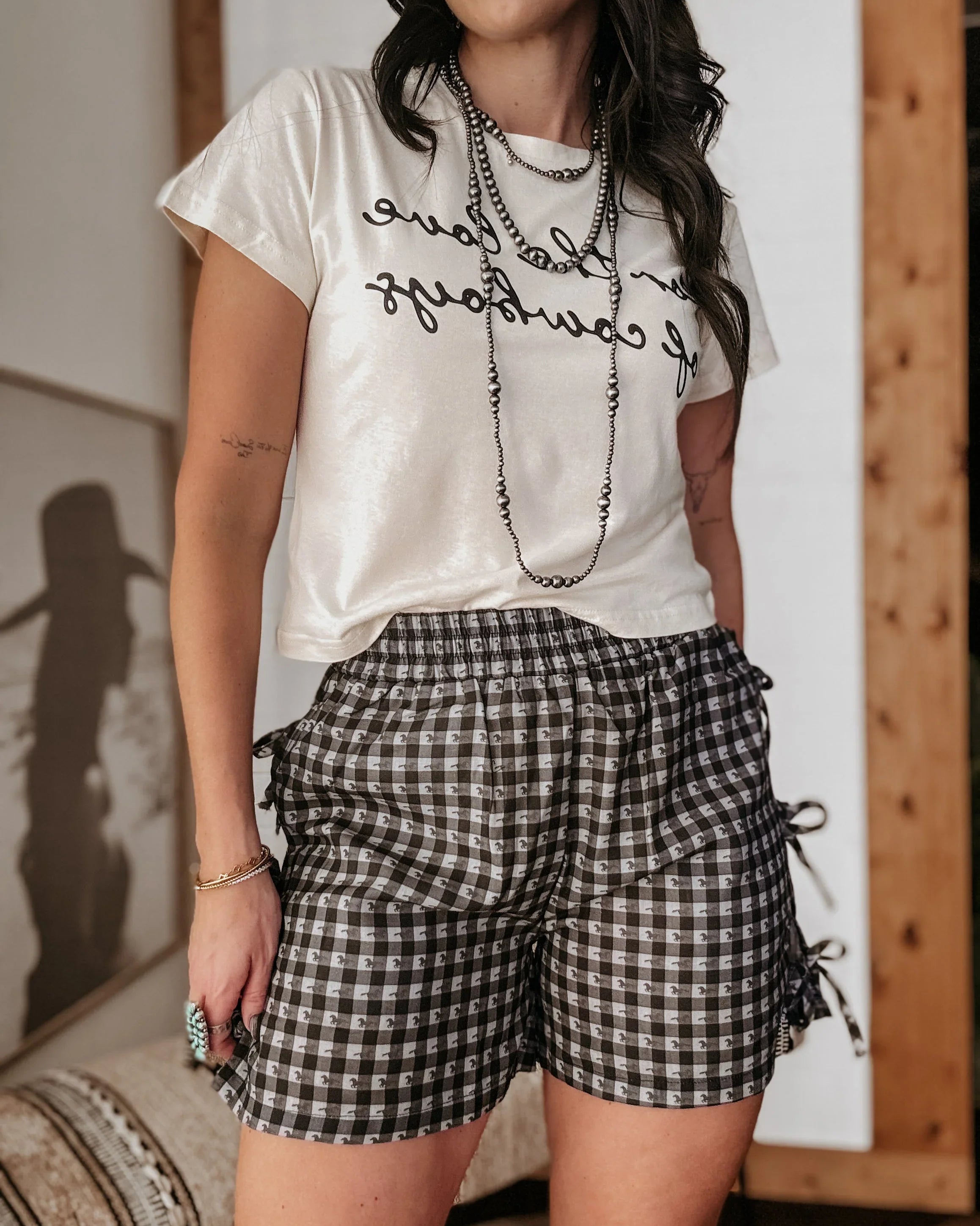 Person wearing a white t-shirt with text and black and white checkered shorts indoors.