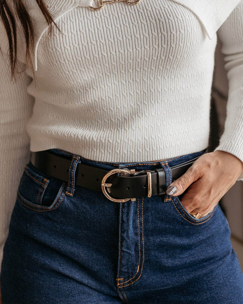 Woman wearing a white ribbed sweater, high-waisted jeans, and a western black belt with gold buckle