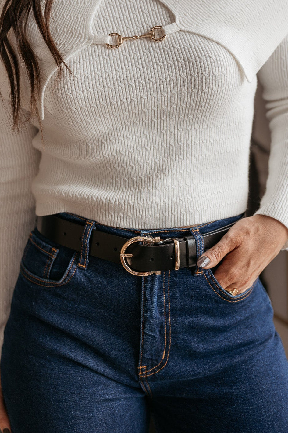 Woman wearing a white ribbed sweater, high-waisted jeans, and a western black belt with gold buckle
