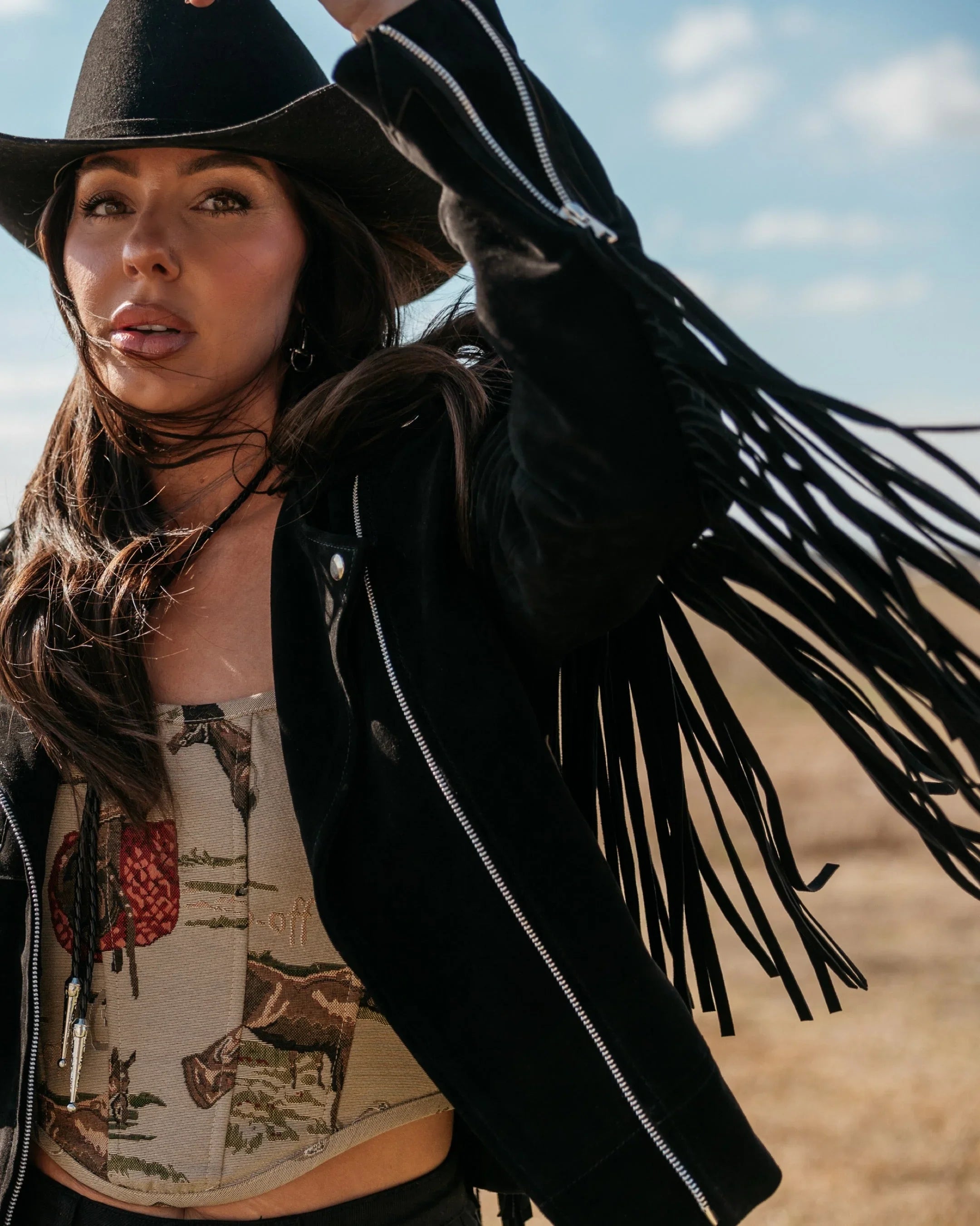 Woman in black cowboy hat and fringe suede jacket, western boho outfit outdoors